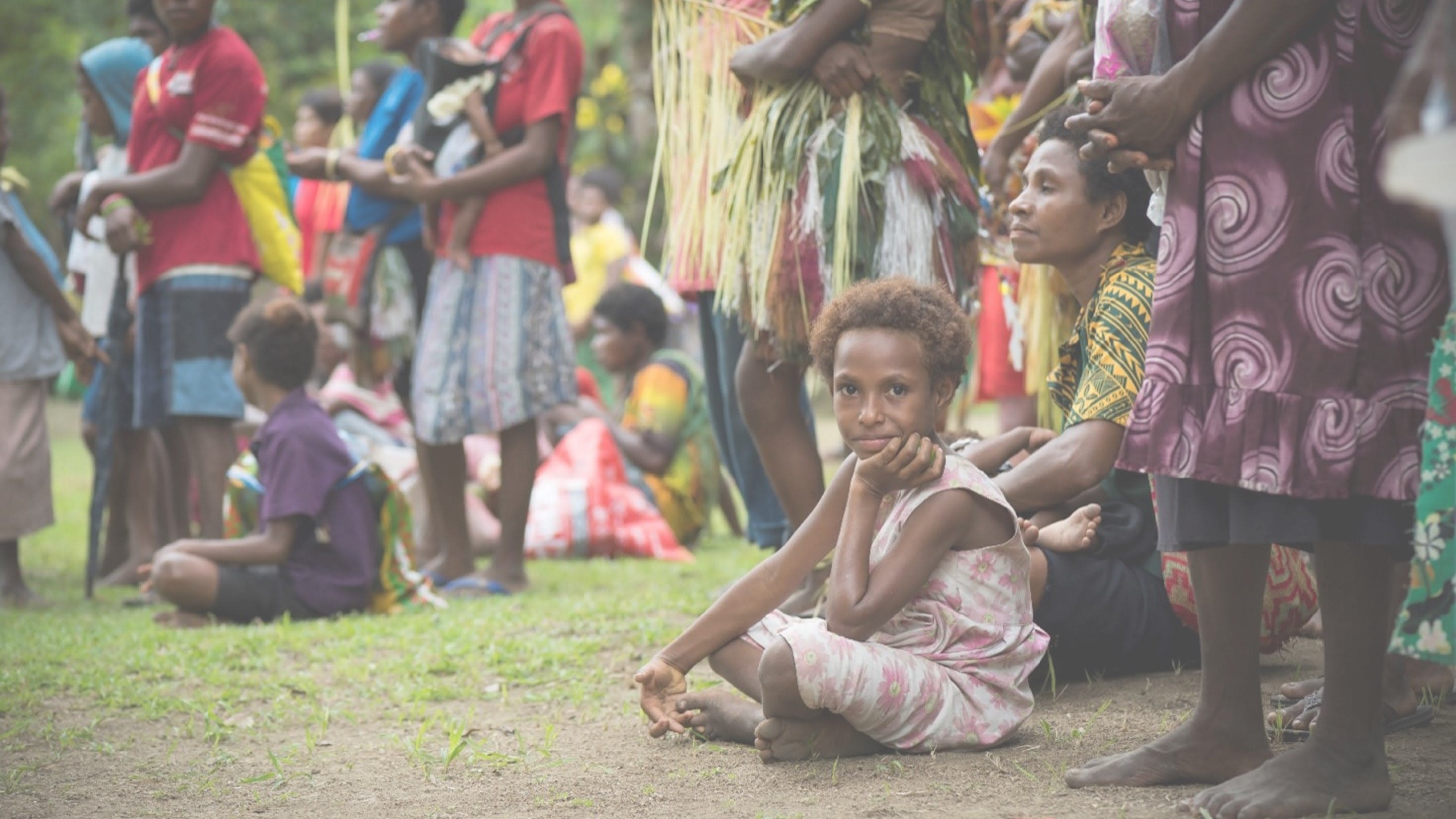A group of community kids and people sitting on the ground