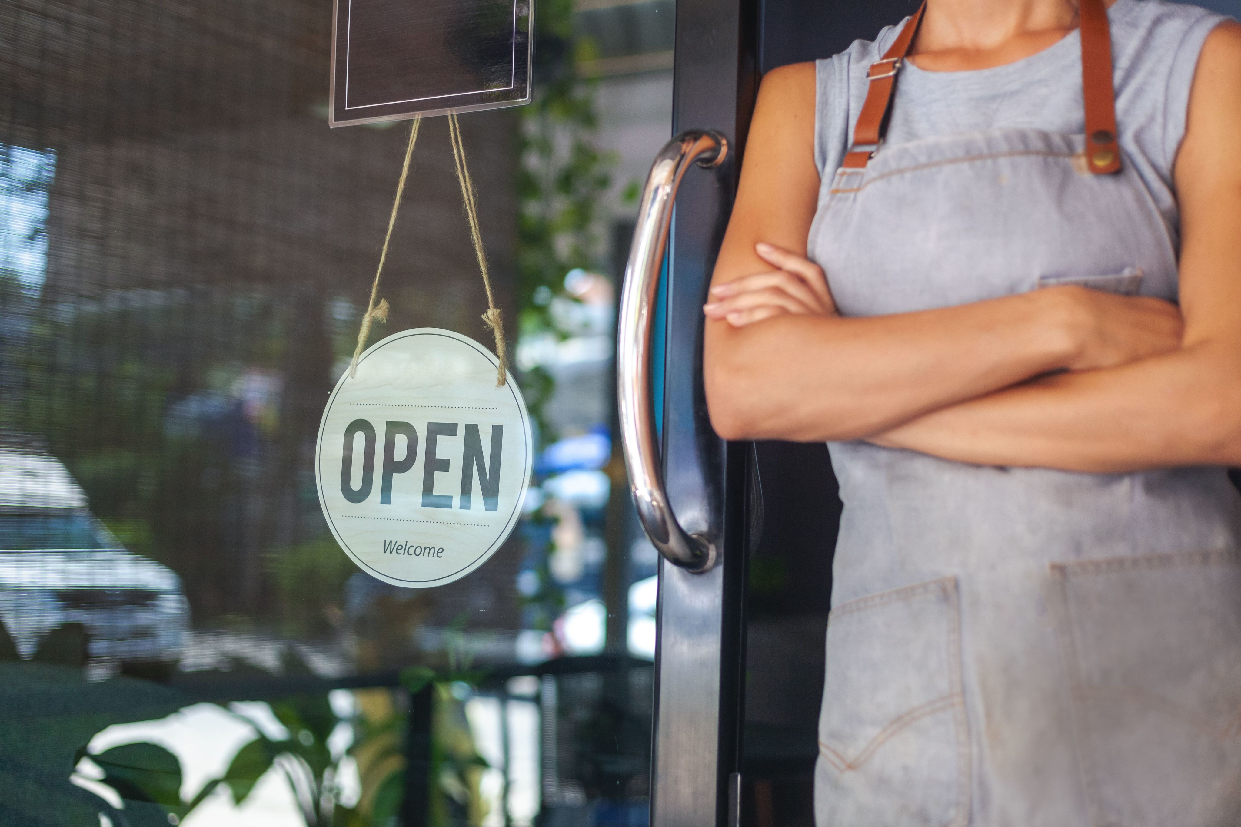 Waitress with an apron standing at the cafe door with an open sign