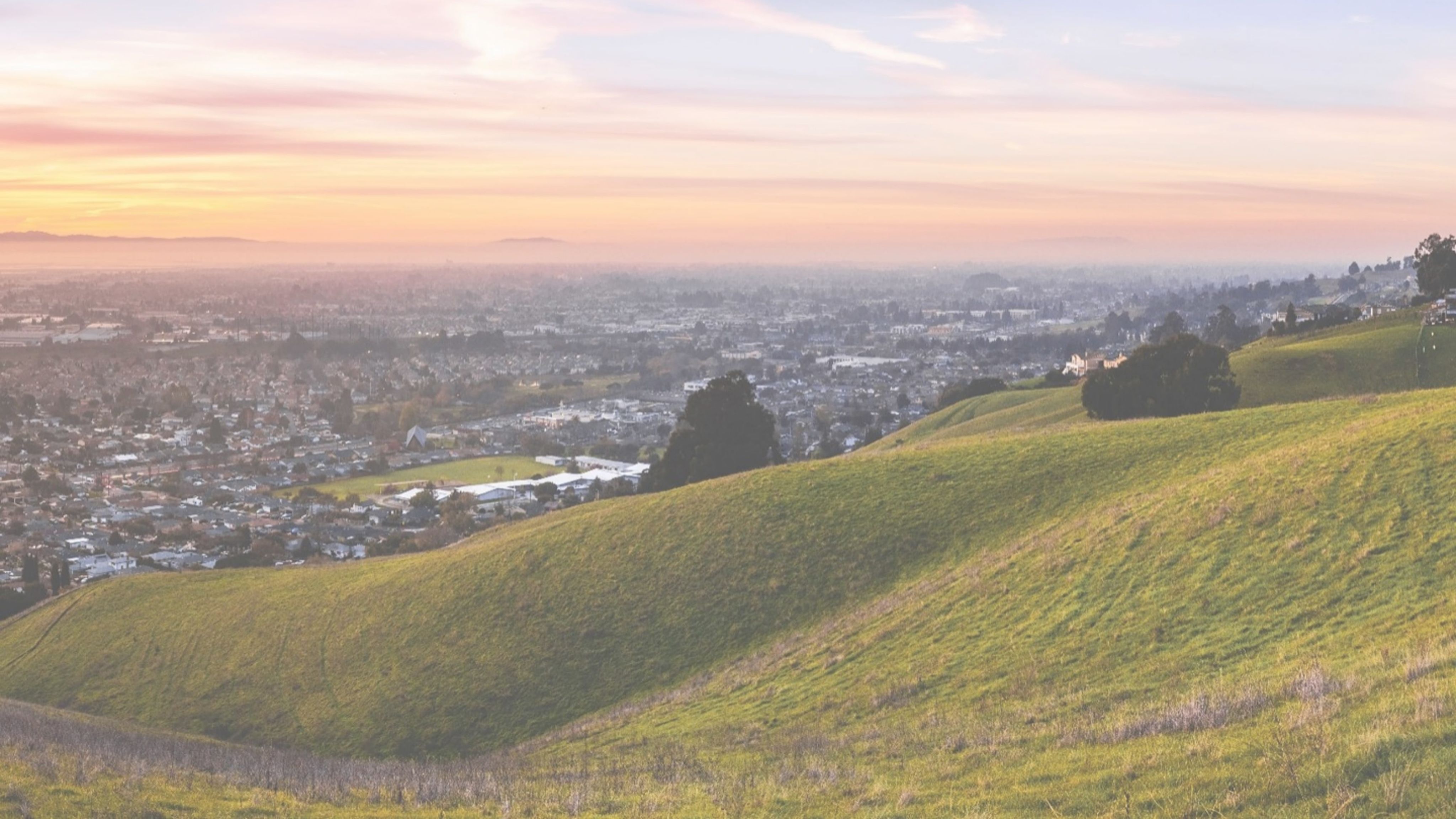 Sunset view of hiking trail on the verdant hills of East San Francisco Bay Area; the city of Hayward and the bay visible in the valley; California.
