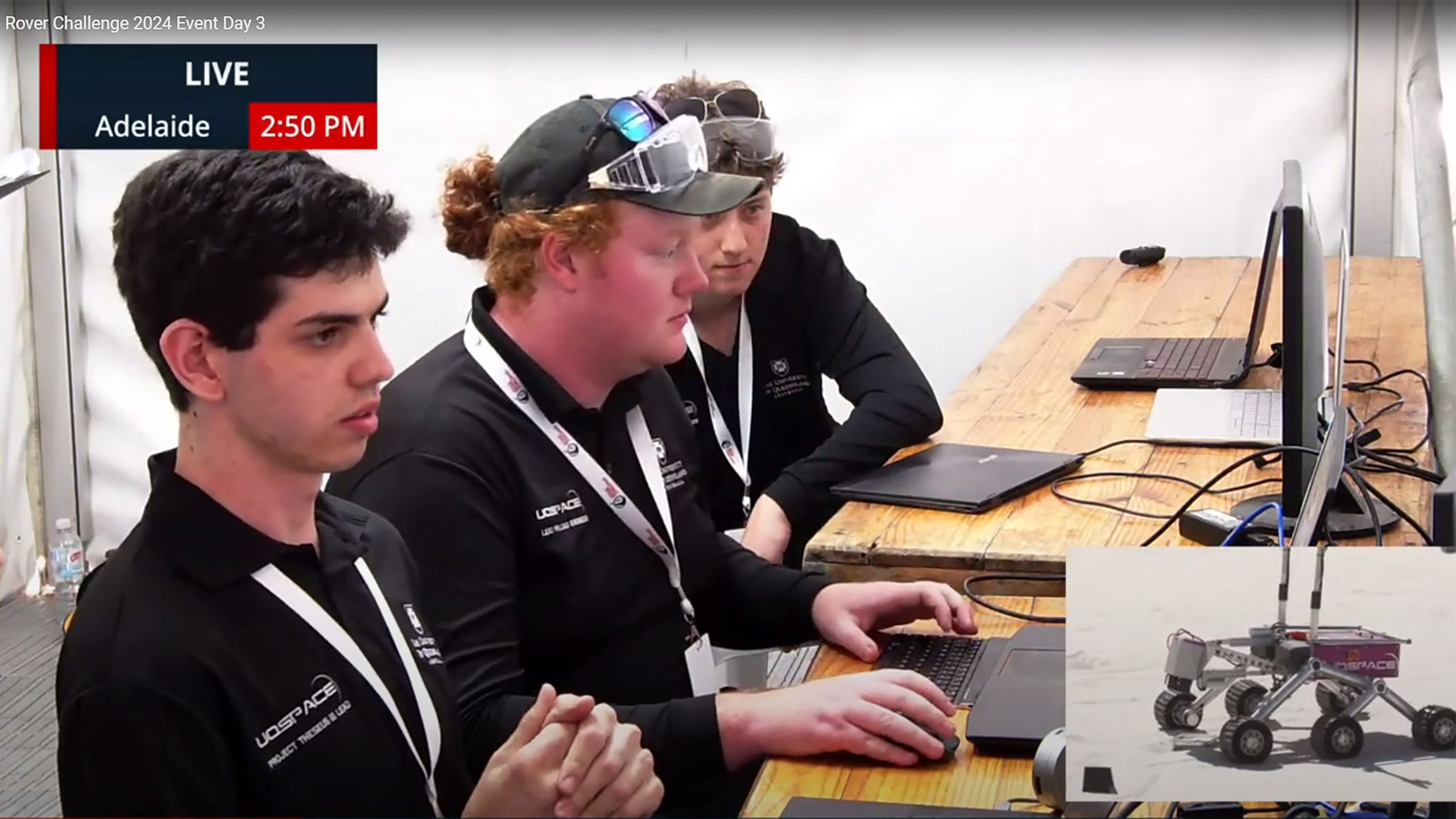 A screenshot from a video where three men are sitting at a desk using computers