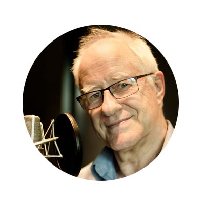 Image of a headshot of an older man with white hair and glasses, he is smiling and had a microphone next to him