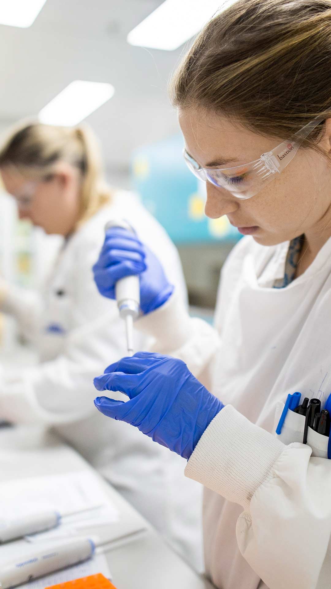 COVID-19 research lab, women holding testing equipment and wearing glasses and lab coat