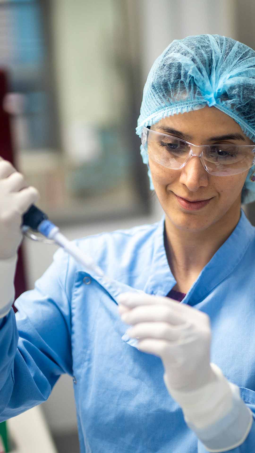 COVID-19 research lab, women holding testing equipment and wearing glasses, hair net and blue lab coat
