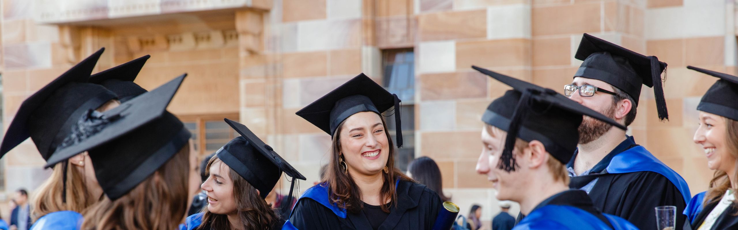 Image of graduates throwing their graduation caps in the air in the Great Court at St Lucia campus.
