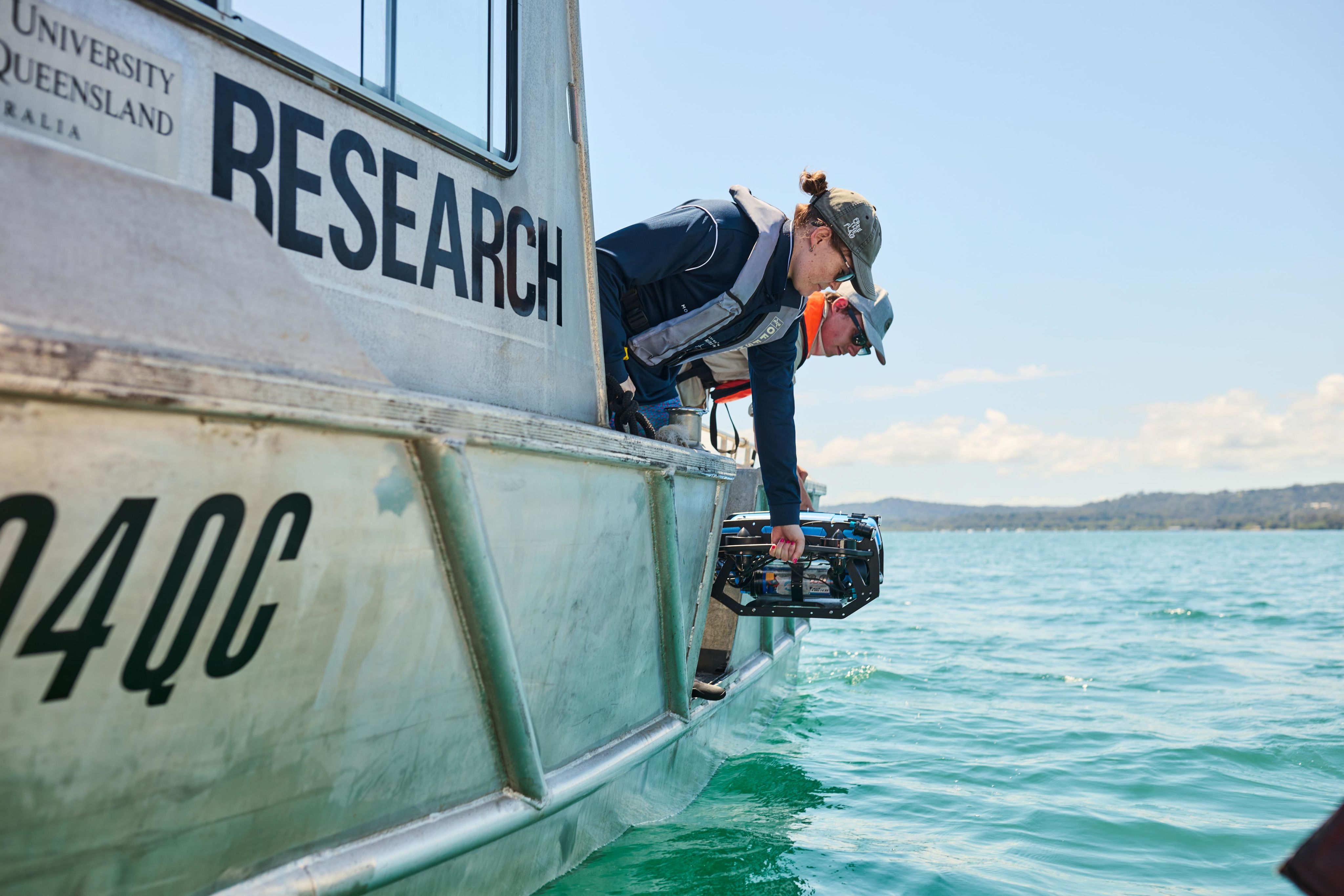 Two researchers on a boat load research equipment into the ocean.