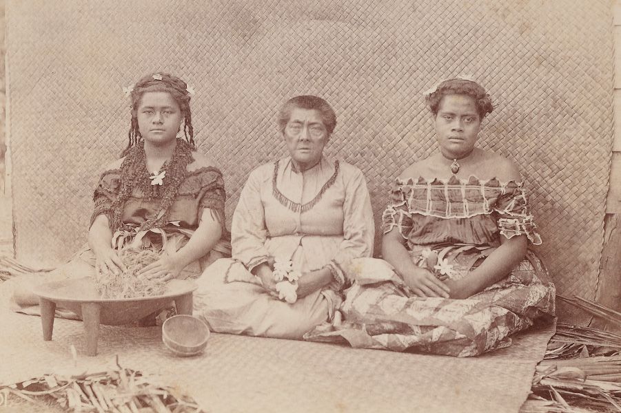 A sepia toned image from around 1880 featuring three Tongan women, seated on woven matting.