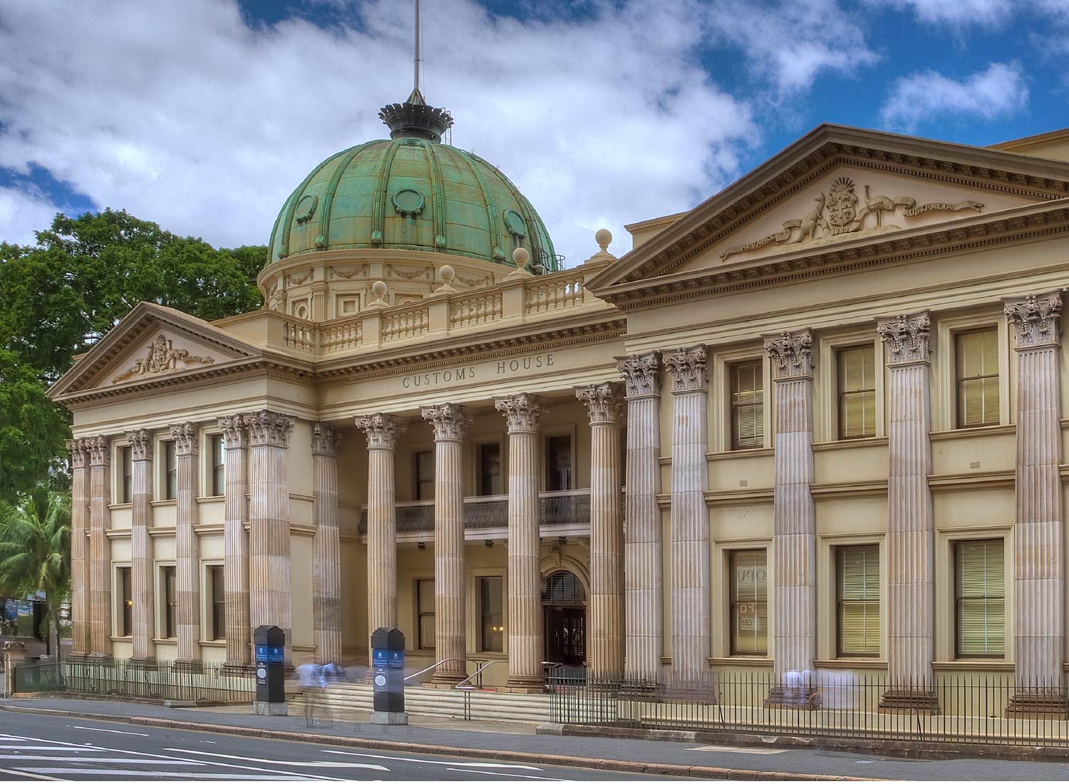 A grand, two-storey sandstone building. Columns adorn the front. A green copper dome protrudes into a blue sky.