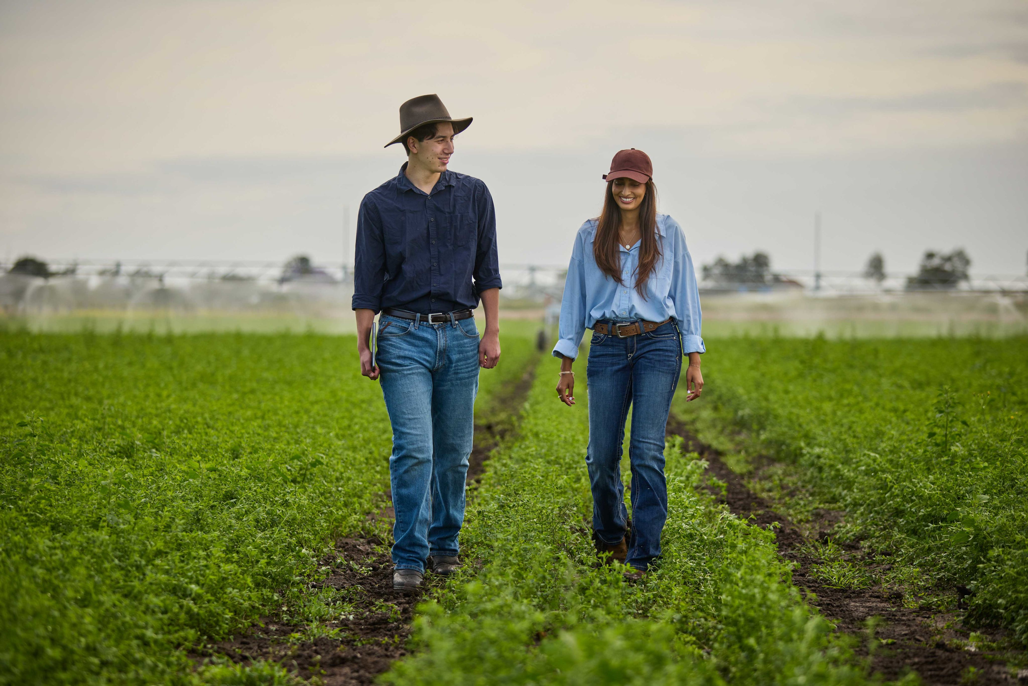 Two students walk through a field at UQ's Gatton campus towards the camera.