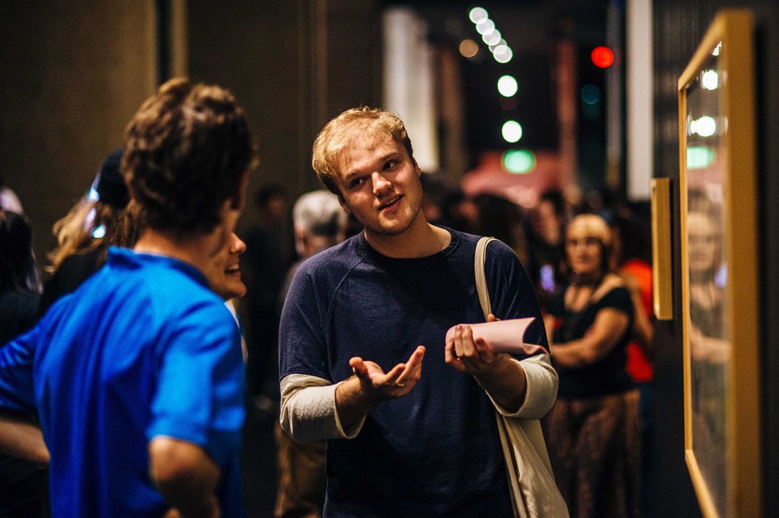 A man in focus gestures to two friends as they discuss an artwork at the Second Sight exhibition opening at UQ Art Museum.