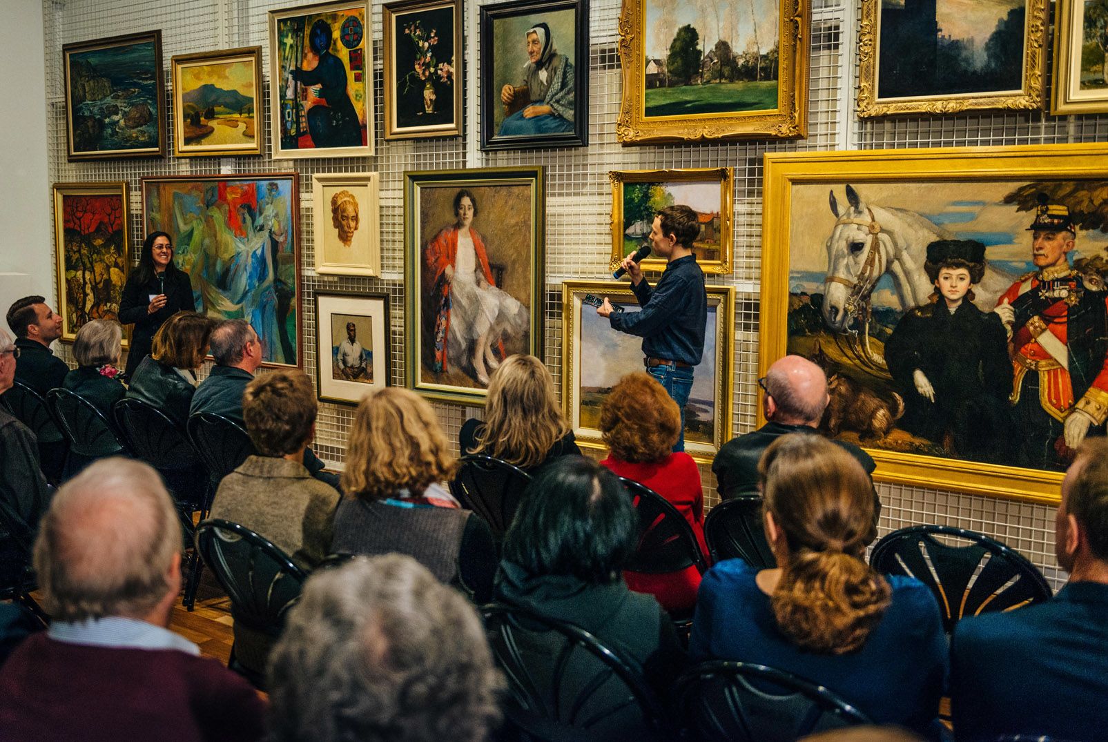 Nikia Tester and Alex Reed present on highlights of the Stuartholme-Behan Collection of Australian Art in front of a selection of artworks and an audience of Art Museum donors in the Collection Study Room.