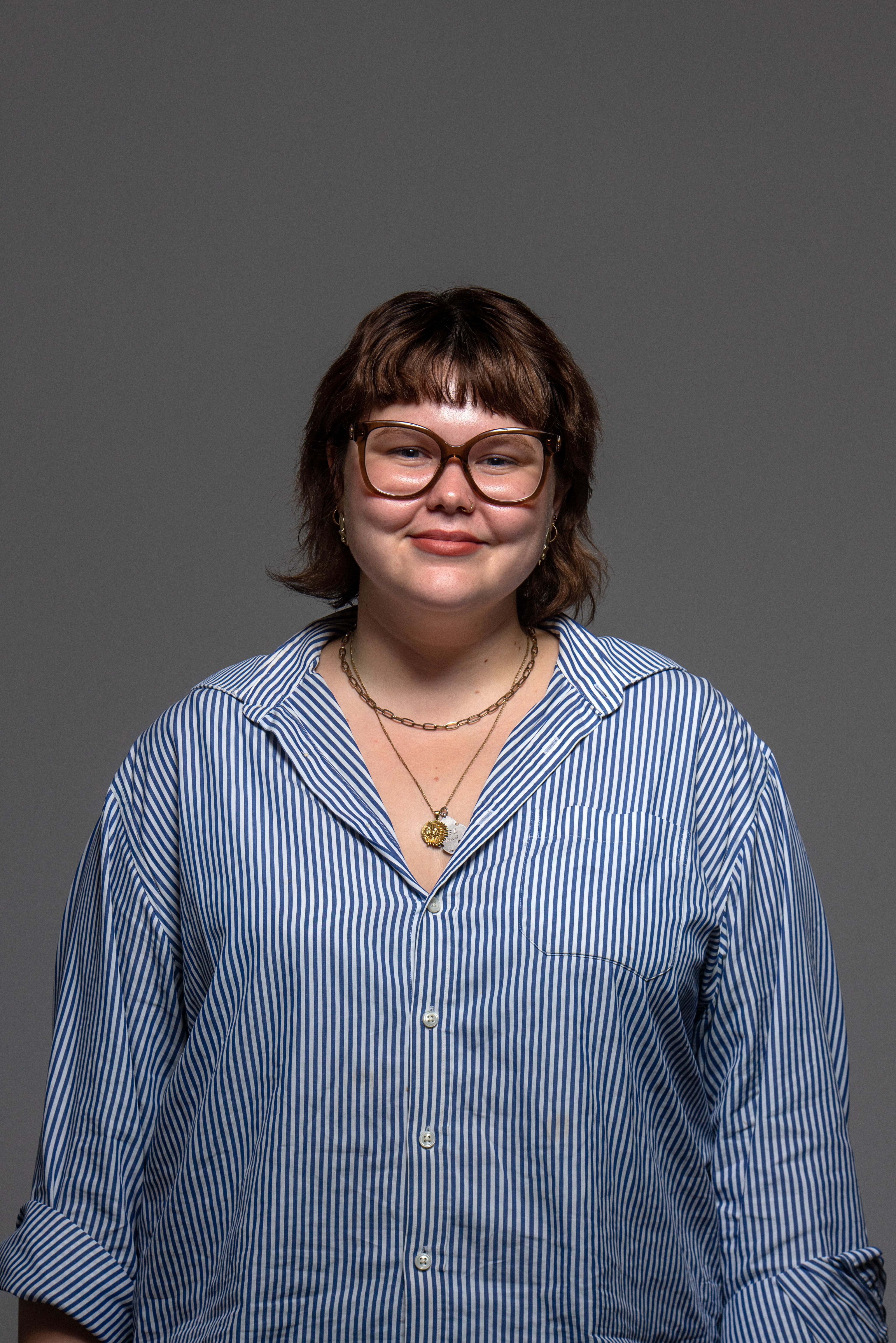 A person with short brown hair and black reading glasses smiling