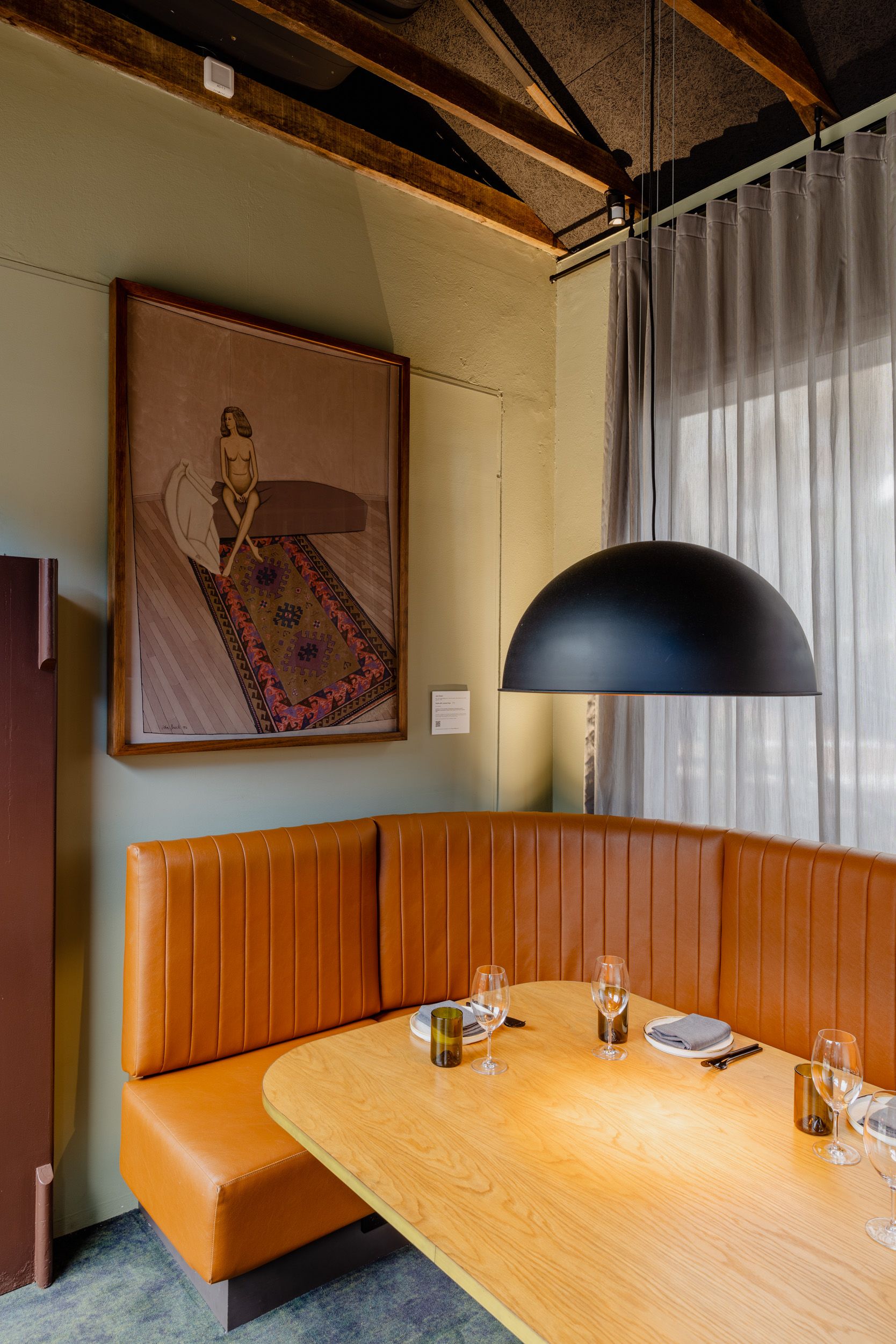 A painting of a nude woman lying on a rug hung above a booth in a restaurant