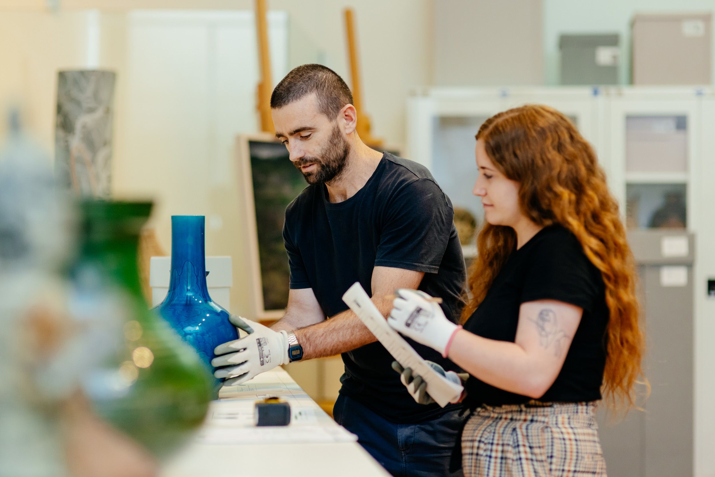Two people wearing gloves looking at vases