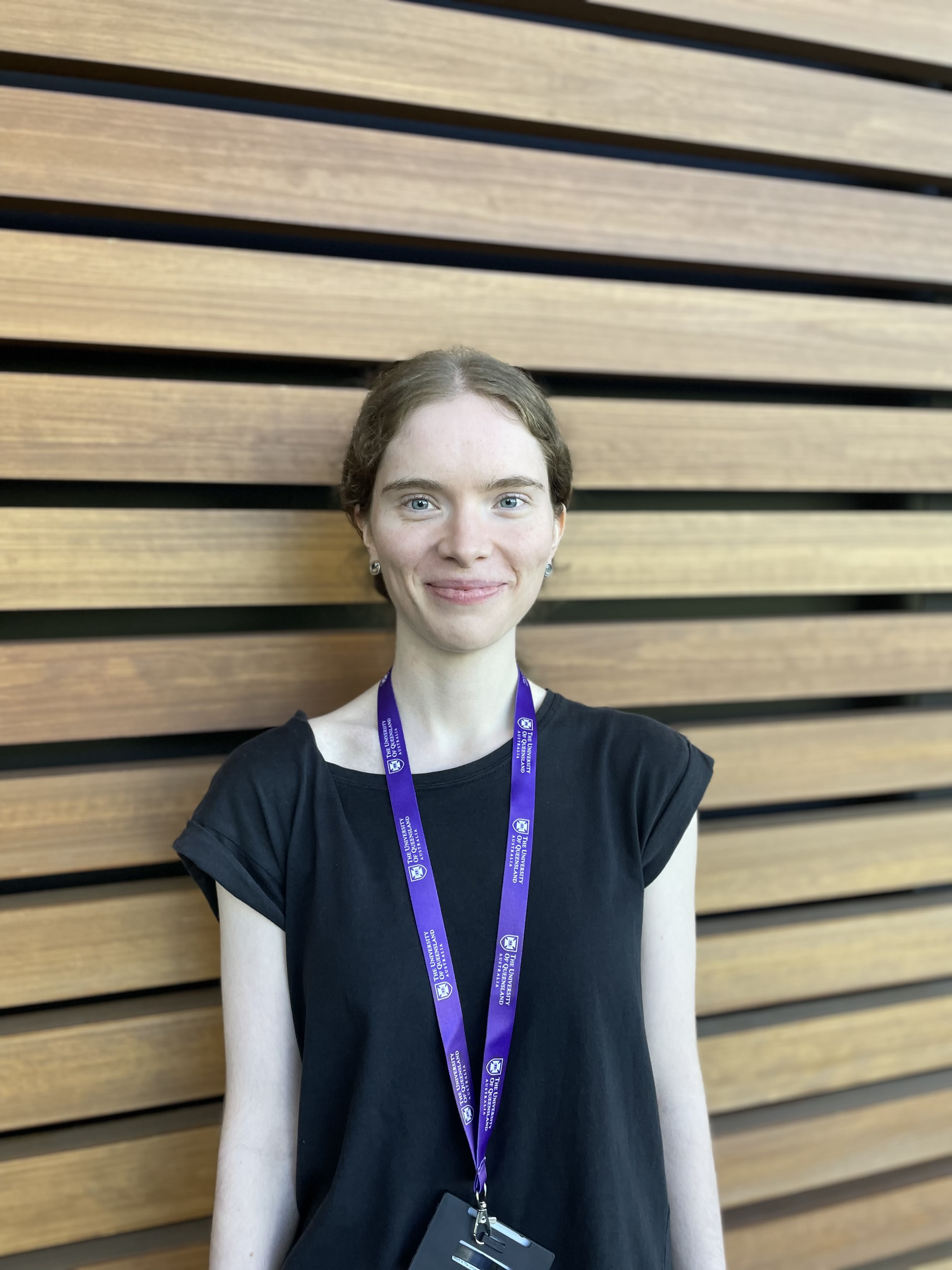A person standing against a wooden slatted wall and smiling