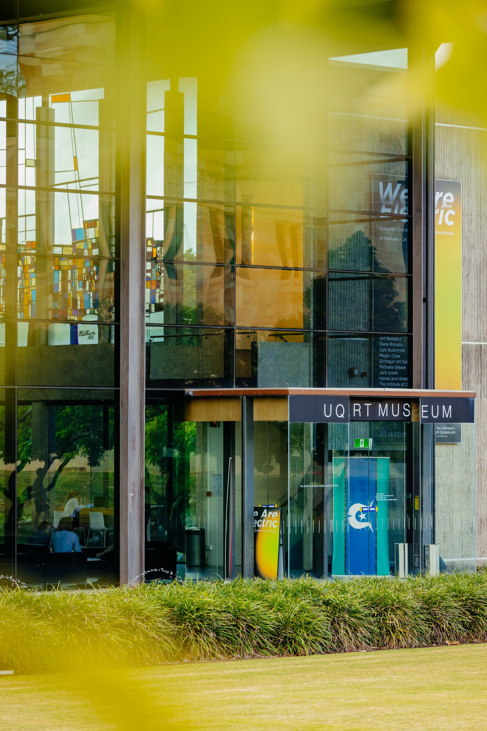 The entrance of a building featuring large glass panels and a sign reading 'UQ Art Museum'
