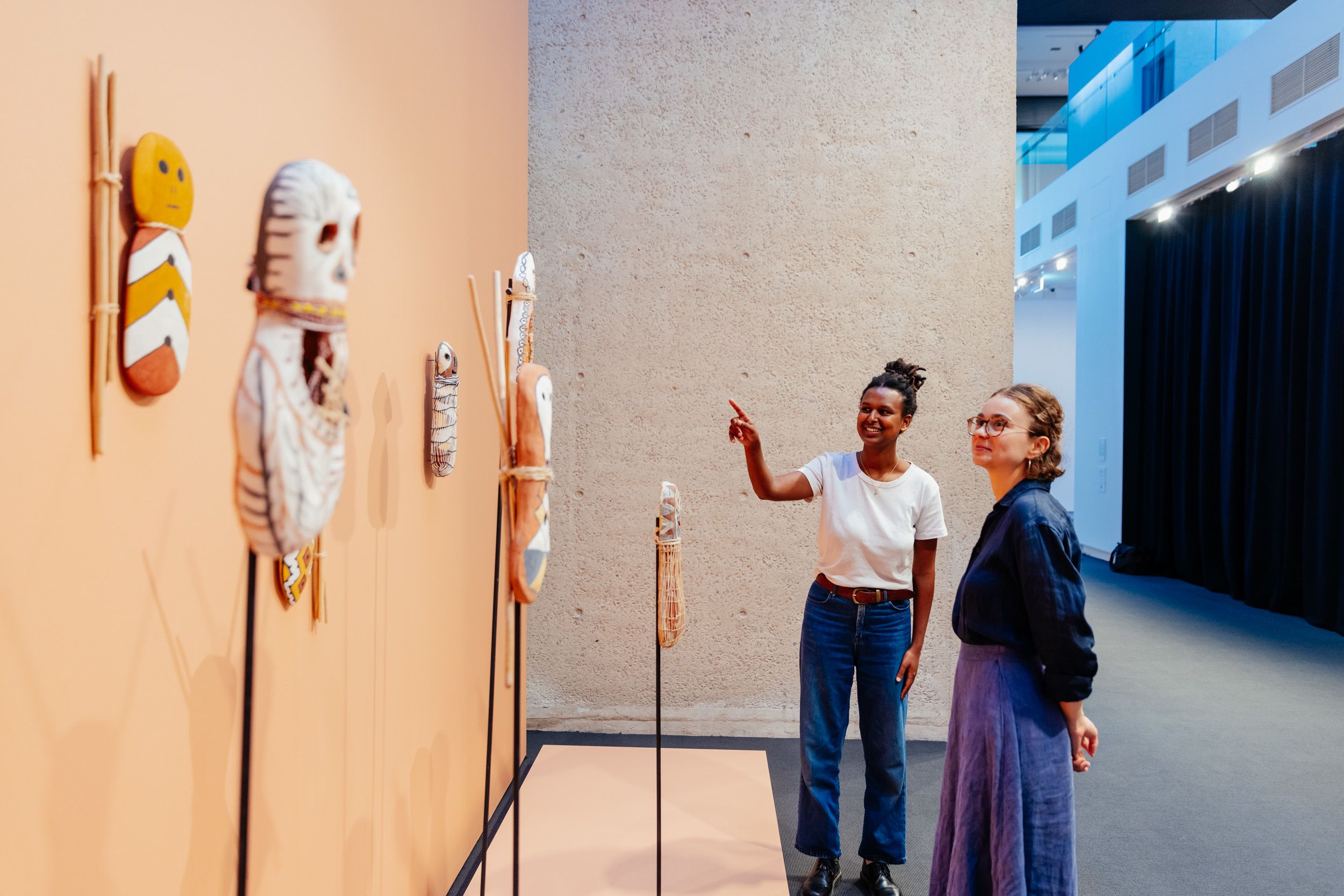Two people standing and looking at a wall displaying a collection of art and small sculptures