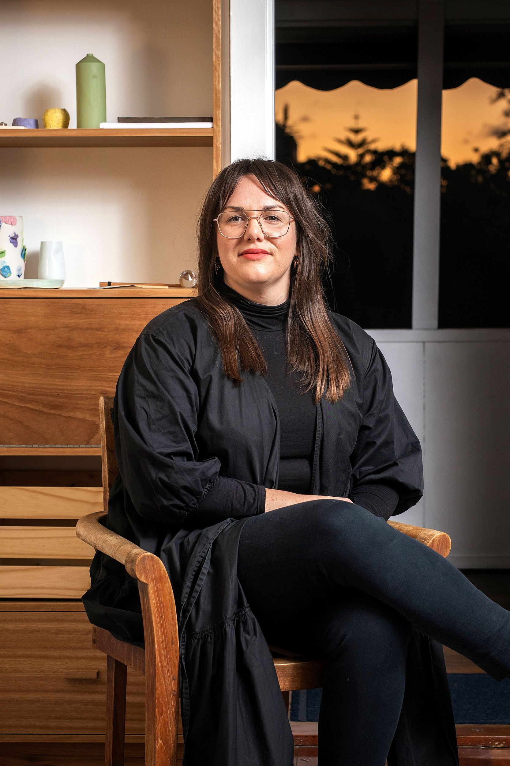 Peta Rake, a woman with long brown hair and dark clothes, sitting in a wooden chair and smiling