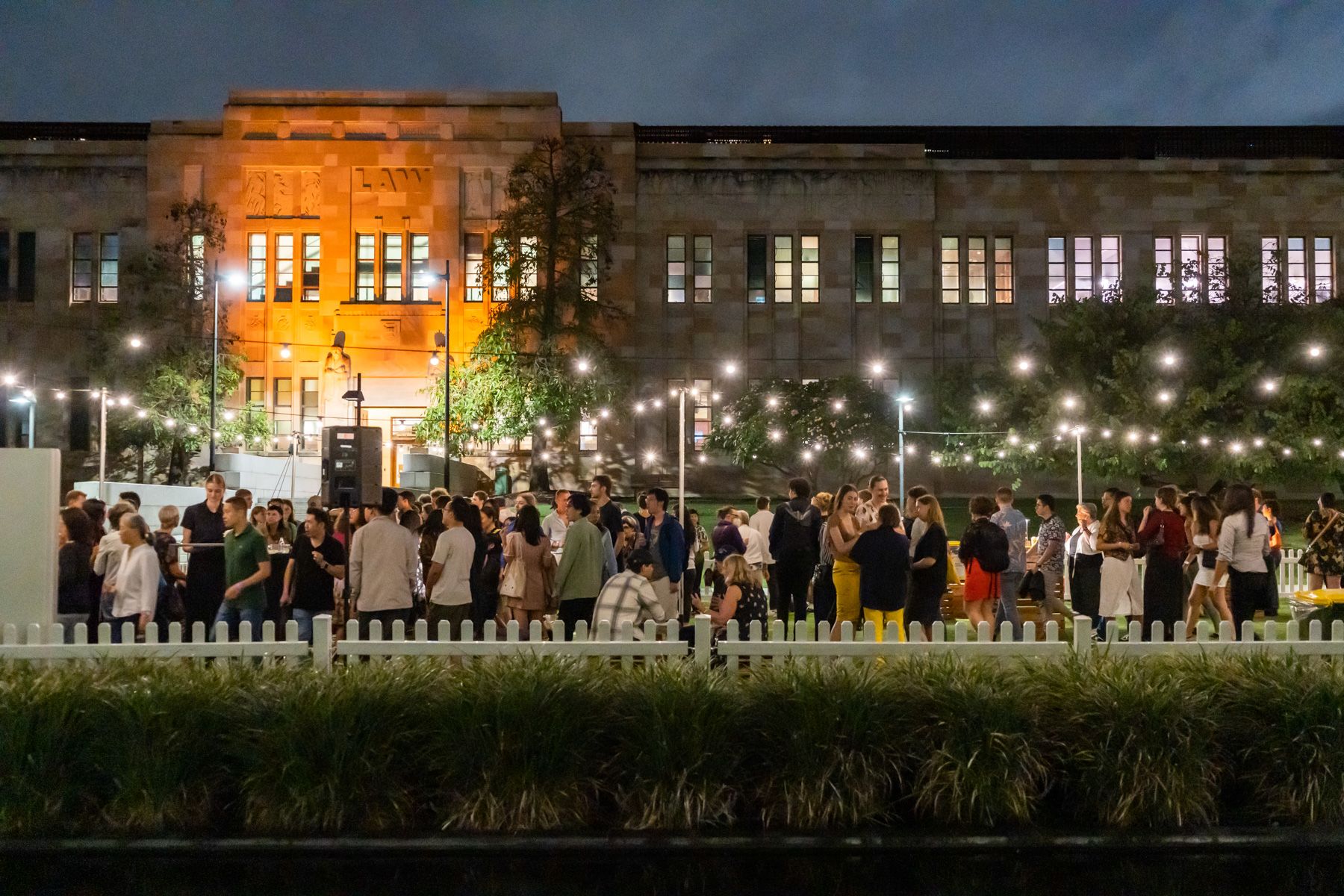 A large group of people standing on a lawn at a night time event