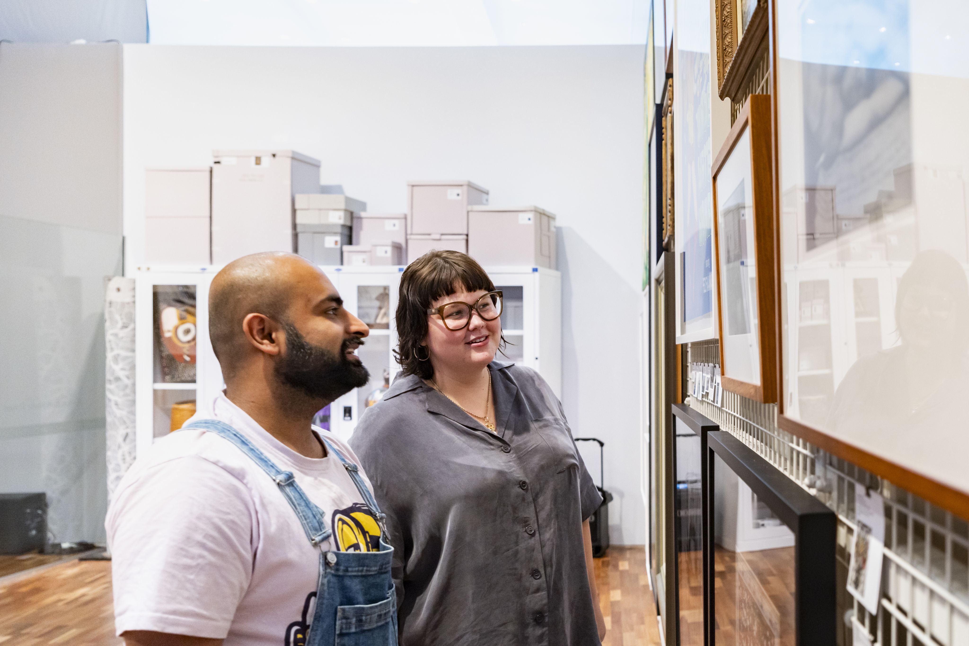 Two people standing by a wall full of artworks hung closely together