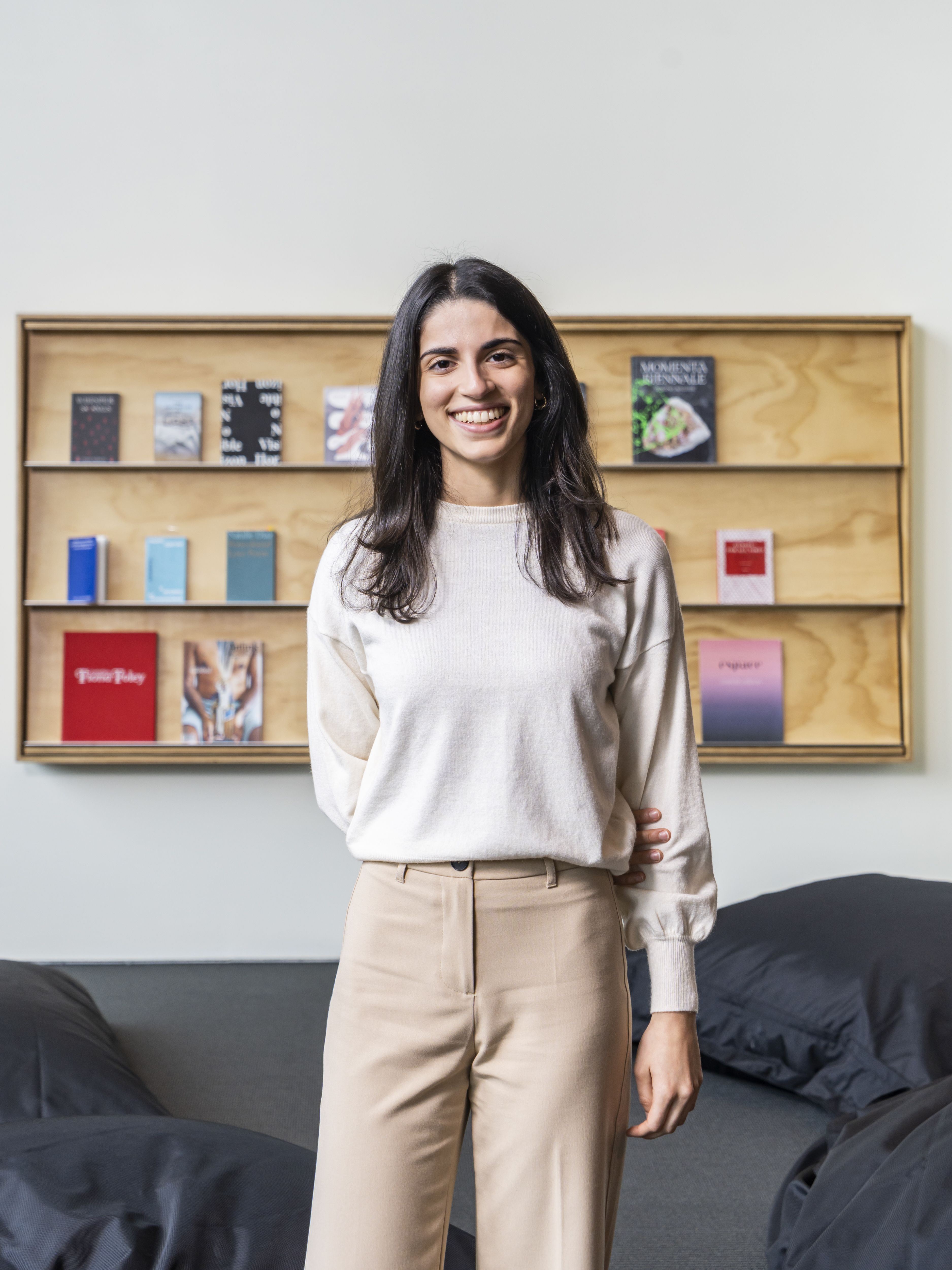 A person standing in front of a wooden bookshelf and smiling