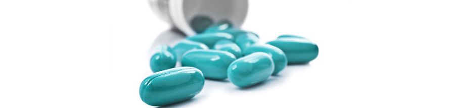 Blue pills an pill bottle on white background. Image Credit: Tish1 