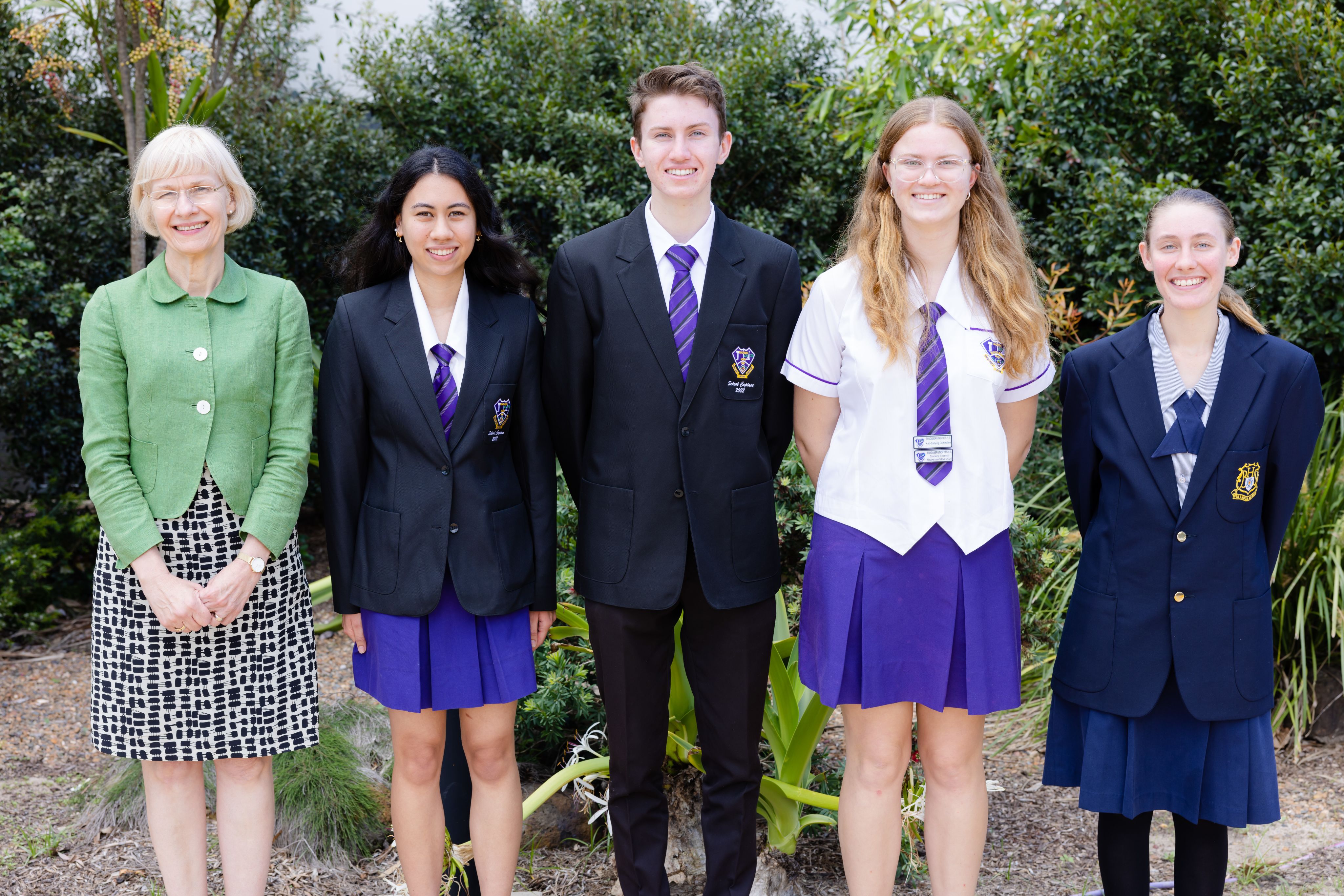 4 students in blue and white school uniforms standing with a woman in a green jacket.