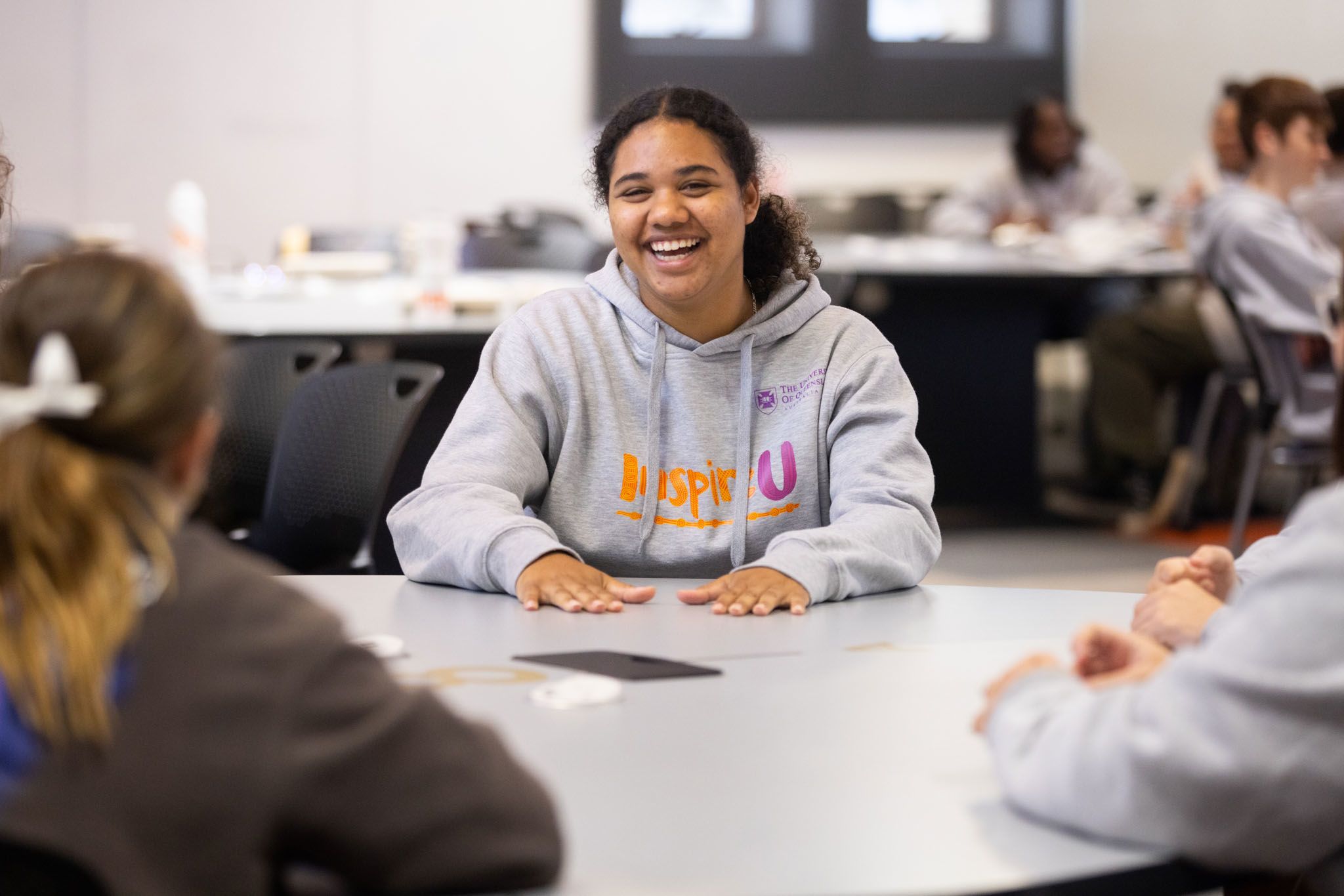 A smiling girl in a grey jumper sitting at a desk