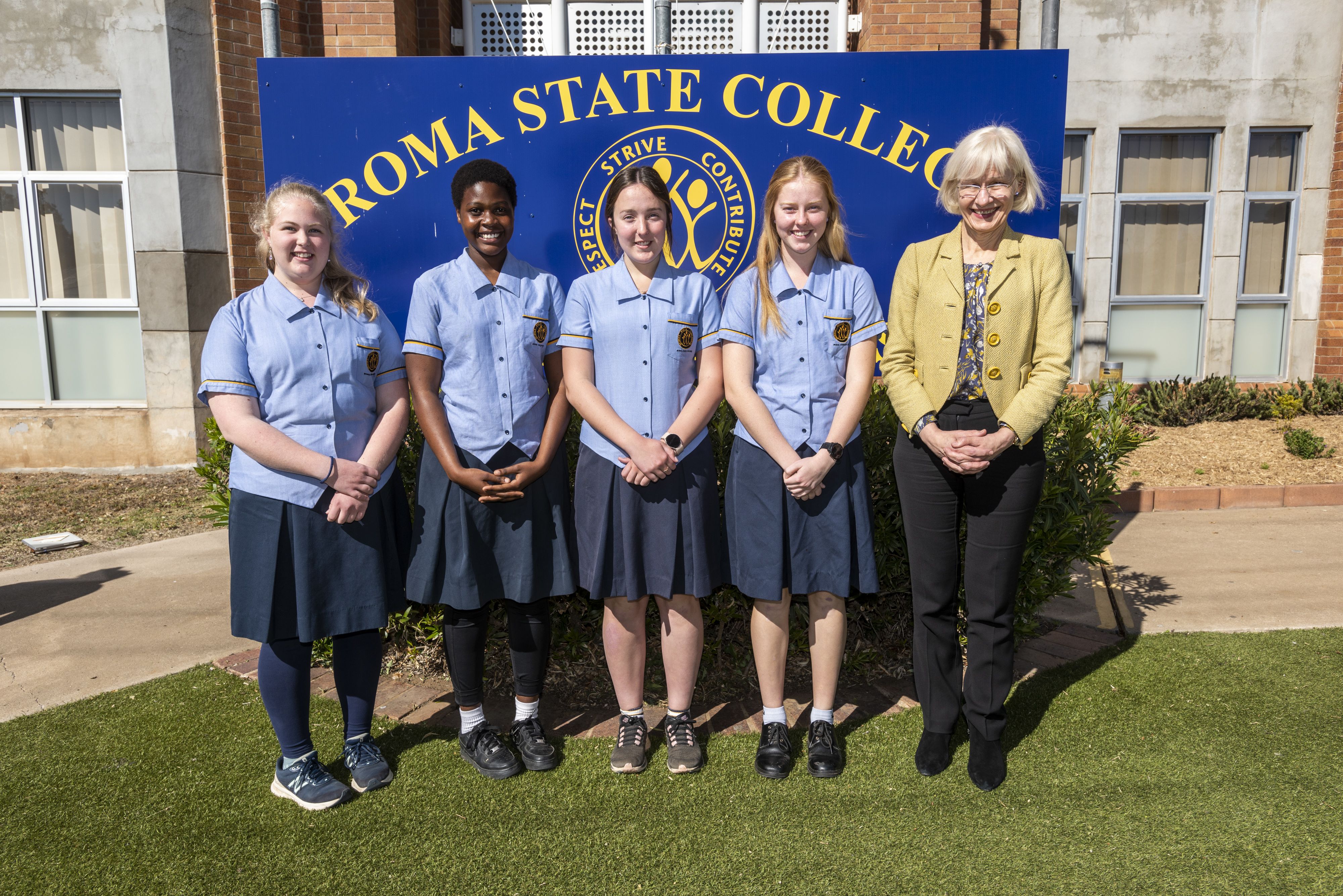 4 students in blue uniforms stand with a woman in a yellow jacket