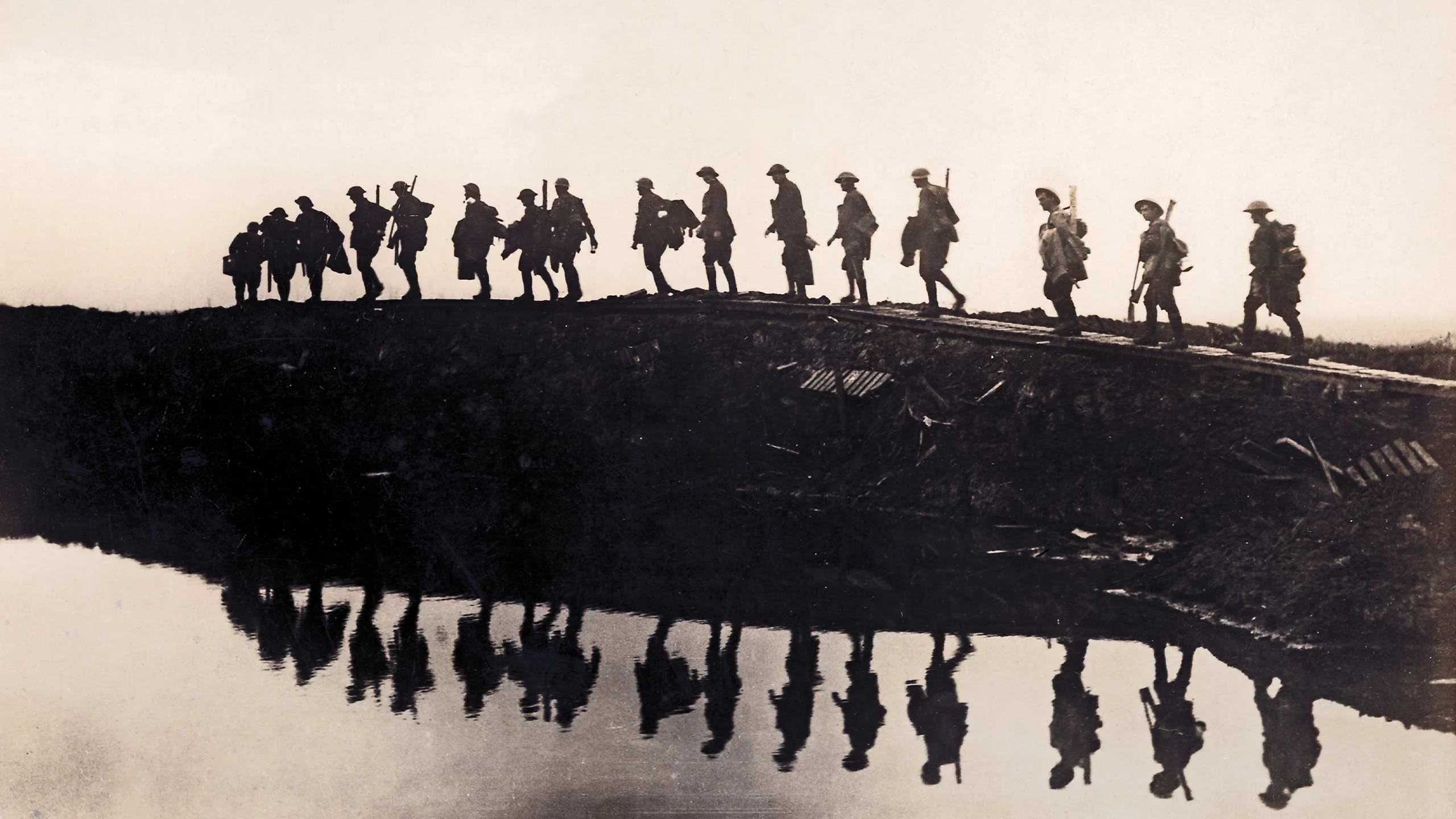 An image of World War 1 soldiers marching over trenches.