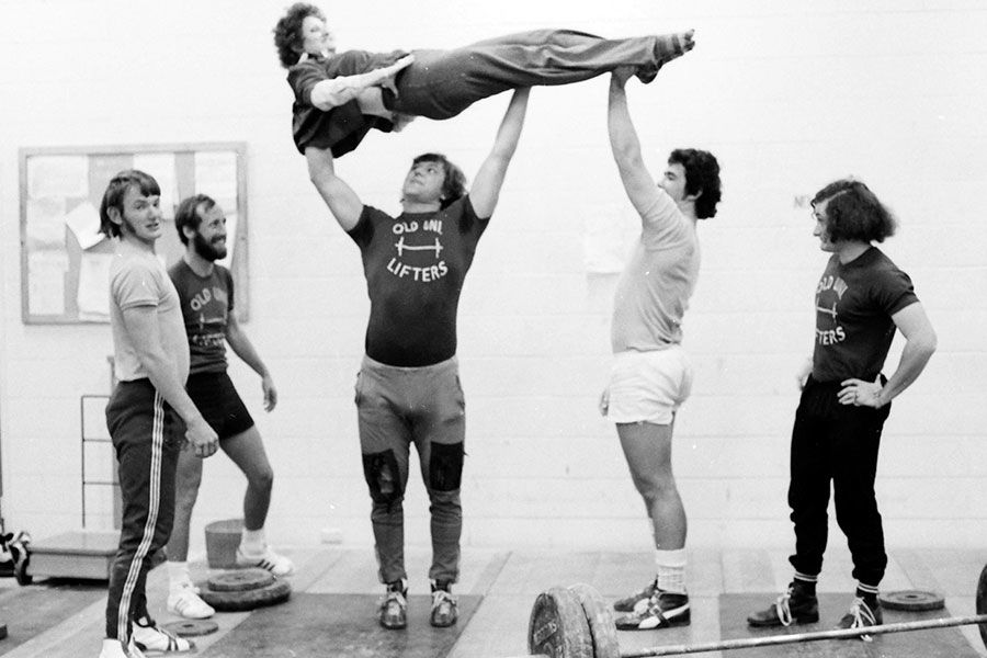 An image of members of the UQ weightlifting team showing off their strength in 1975 by lifting a lady over their heads..