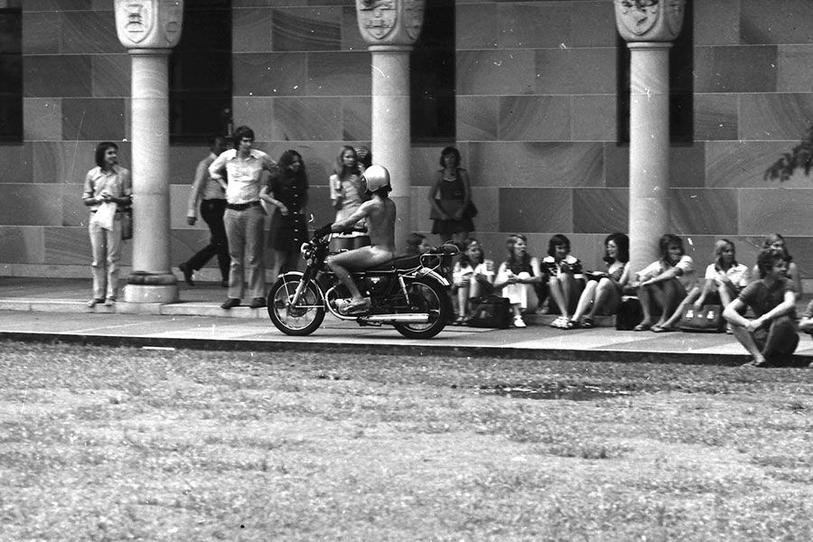 An image of a streaker riding through the Great Court cloisters on a motorbike in 1974.