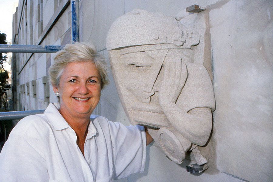 An image of Renowned sculptor Rhyl Hinwood with her self-portrait grotesque at UQ in 1993. Dr Hinwood has spent more than 30 years carving the intricate sandstone artworks that adorn the cloisters of Great Court.