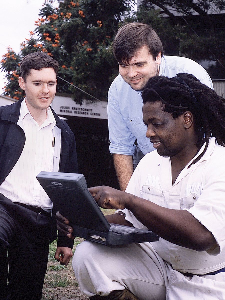 An image of Professor Gideon Chitombo (with laptop) with mineral research colleagues in 1994. Born in Zimbabwe, Professor Chitombo is a leader in university-based international collaborative mining research in the areas of rock breakage by blasting and underground mass mining using caving methods.