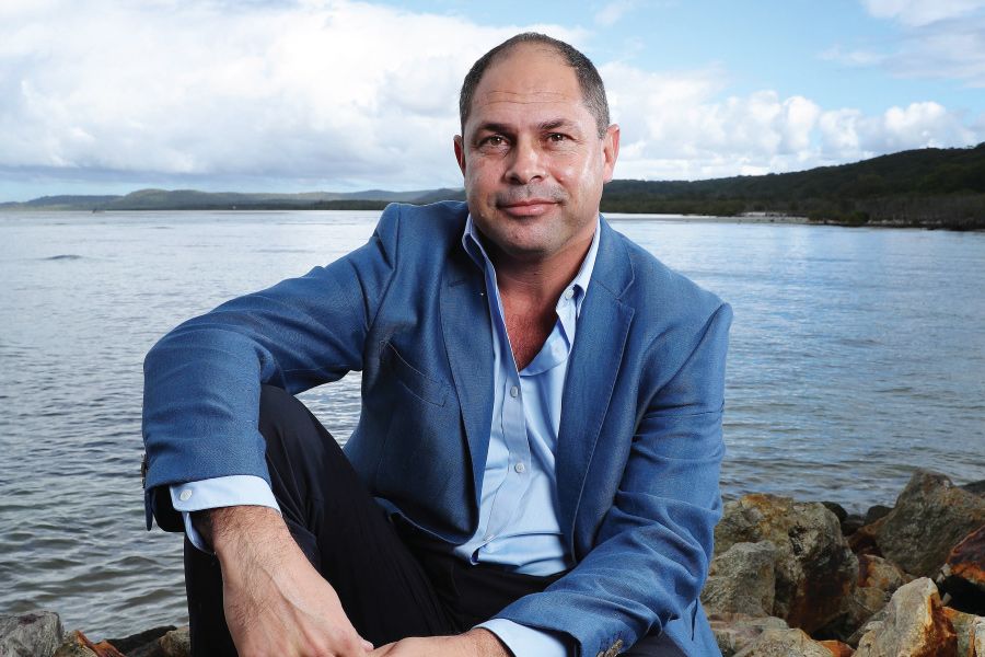 An image of Indigenous Community Impact Award recipient, Cameron Costello sitting on rocks beside the ocean.