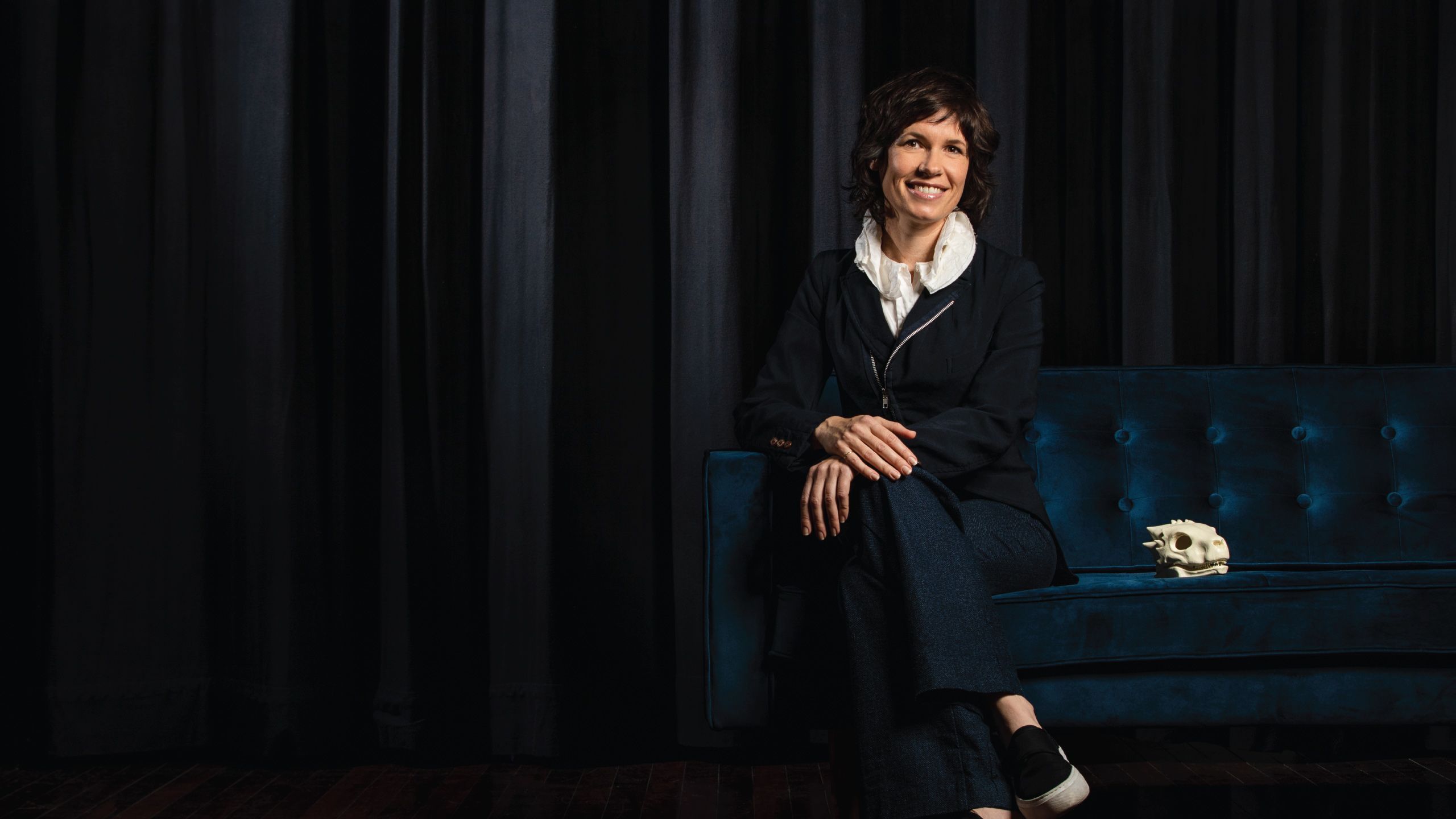 An image of UQ Vice-Chancellor's Alumni Excellence Award recipient, Deborah Riley sitting on a dark couch in a darkened room.