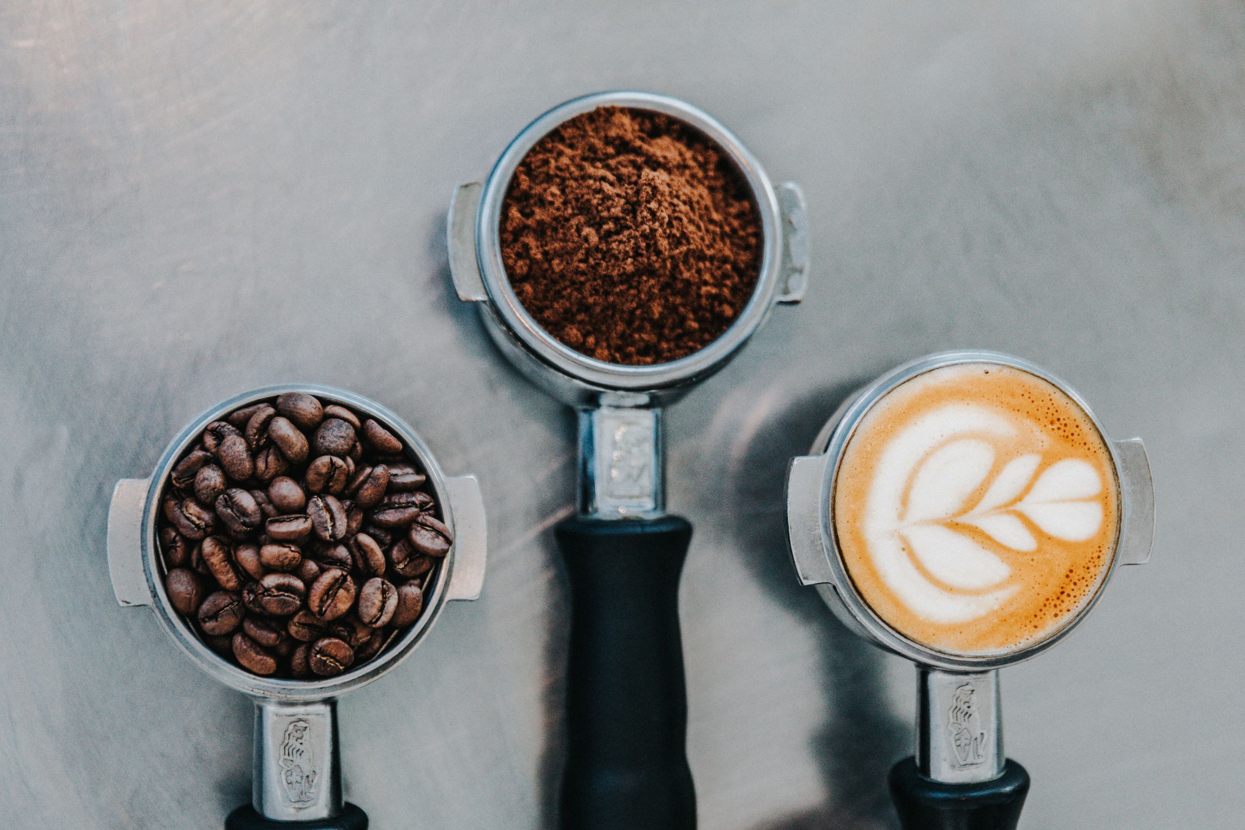 Photo of coffee beans, ground coffee and a coffee with milk