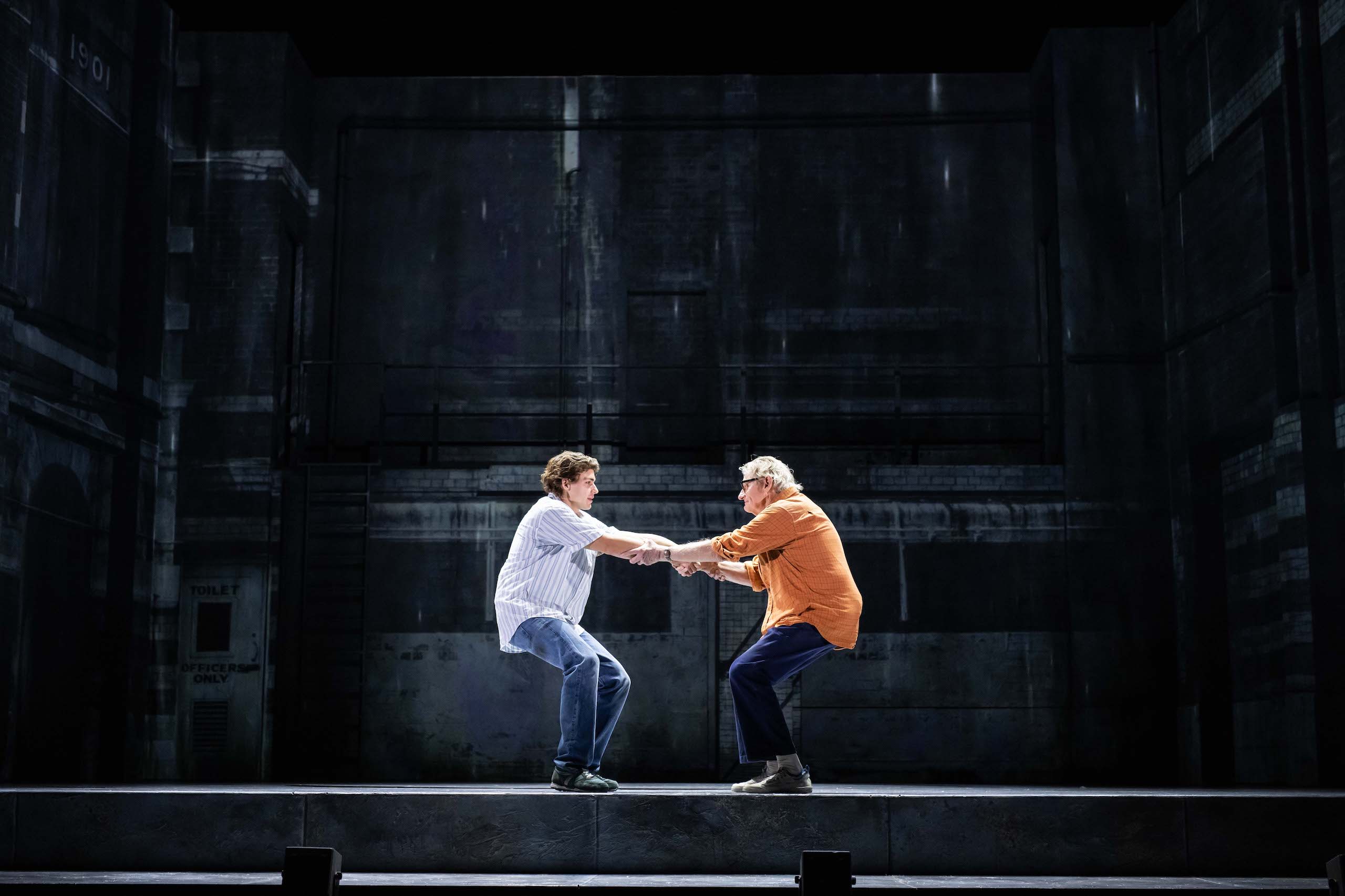 Two men grapple onstage, lit dramatically by an overhead spotlight.