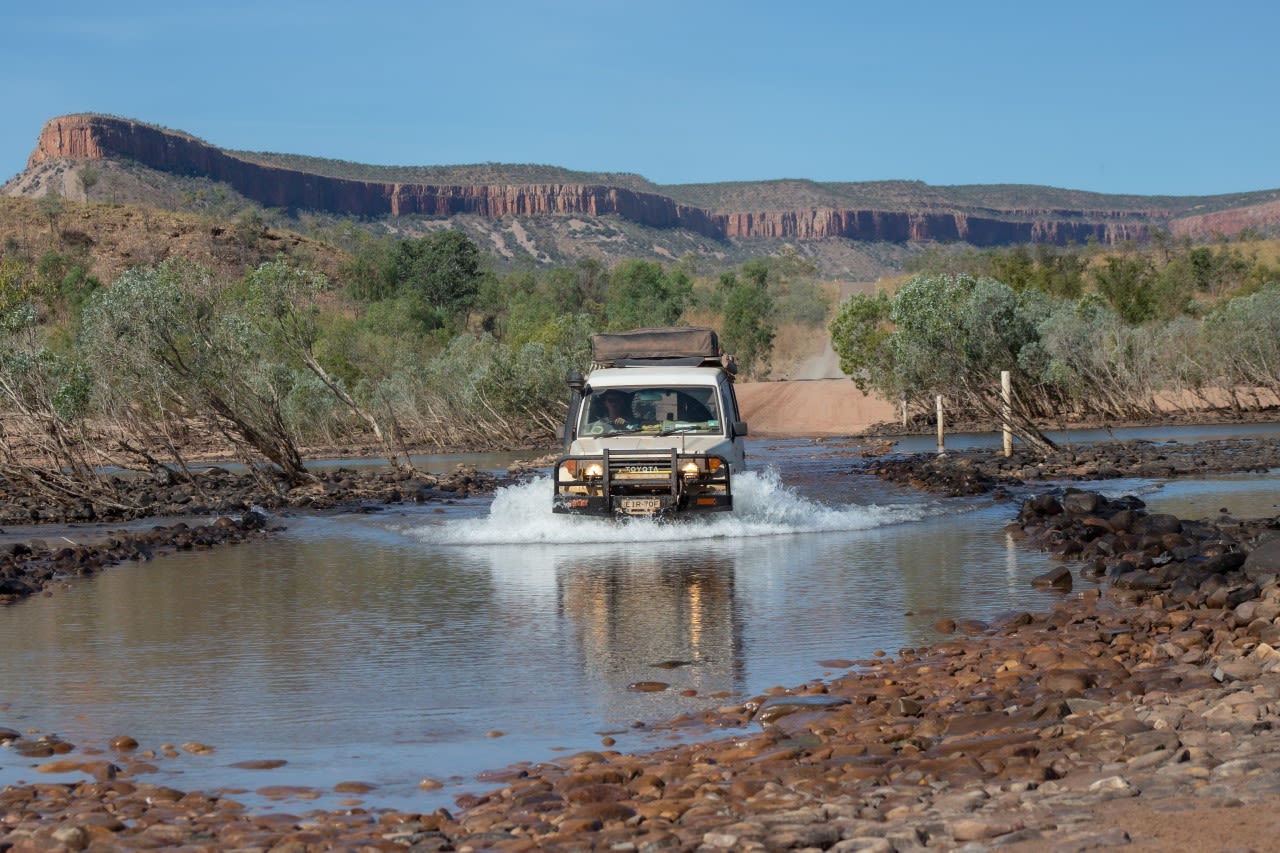 A white Toyota Landcruiser driving across a river in outback Western Australia.