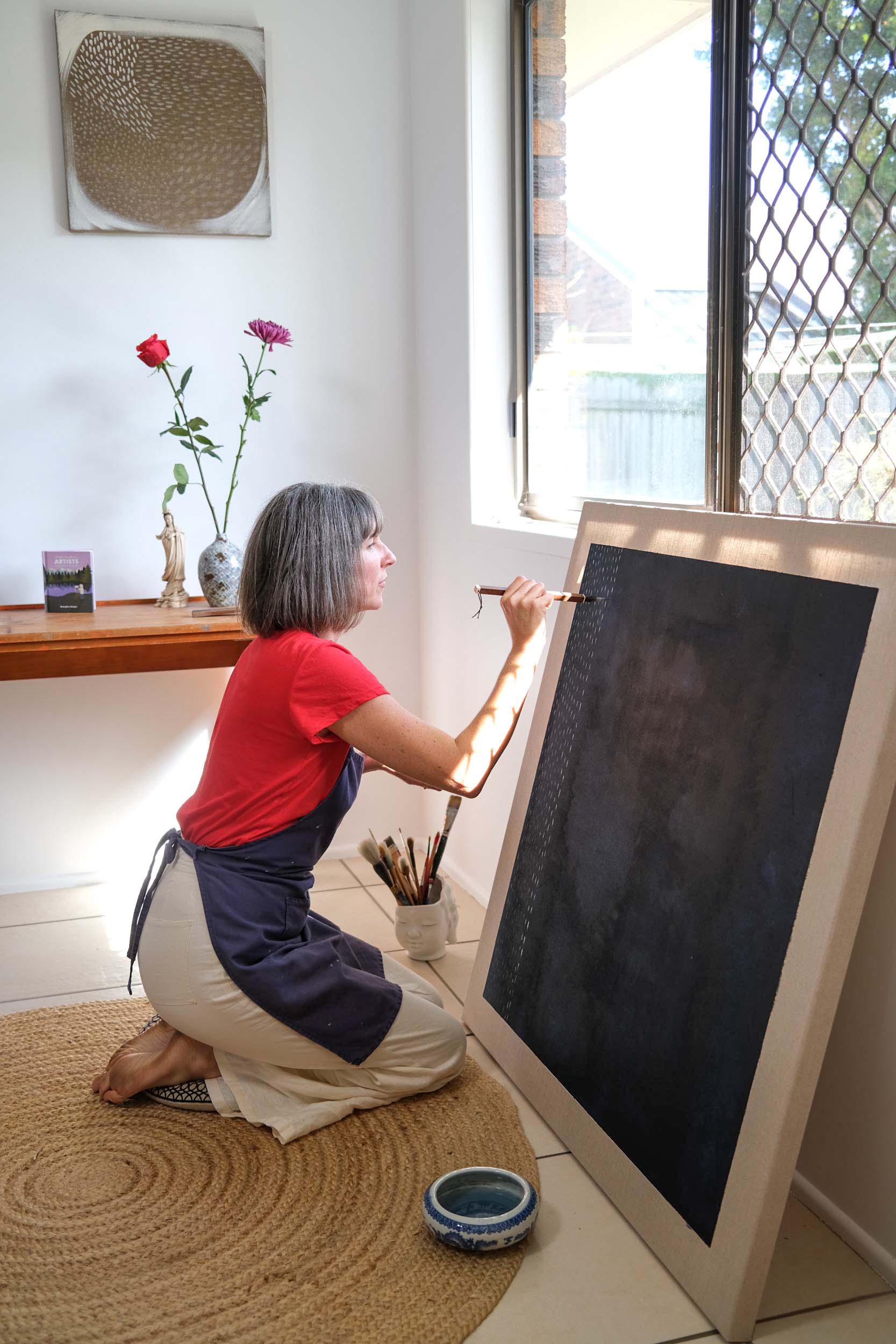 Artist Georgina Hooper painting on a dark indigo canvas.