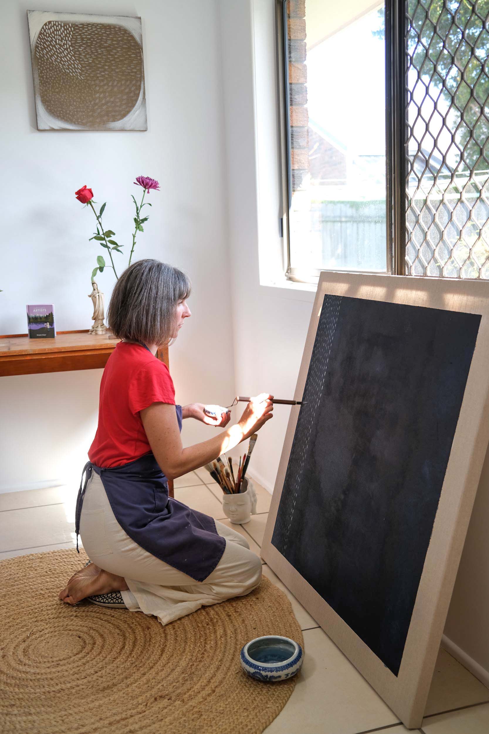 Artist Georgina Hooper painting on a dark indigo canvas.