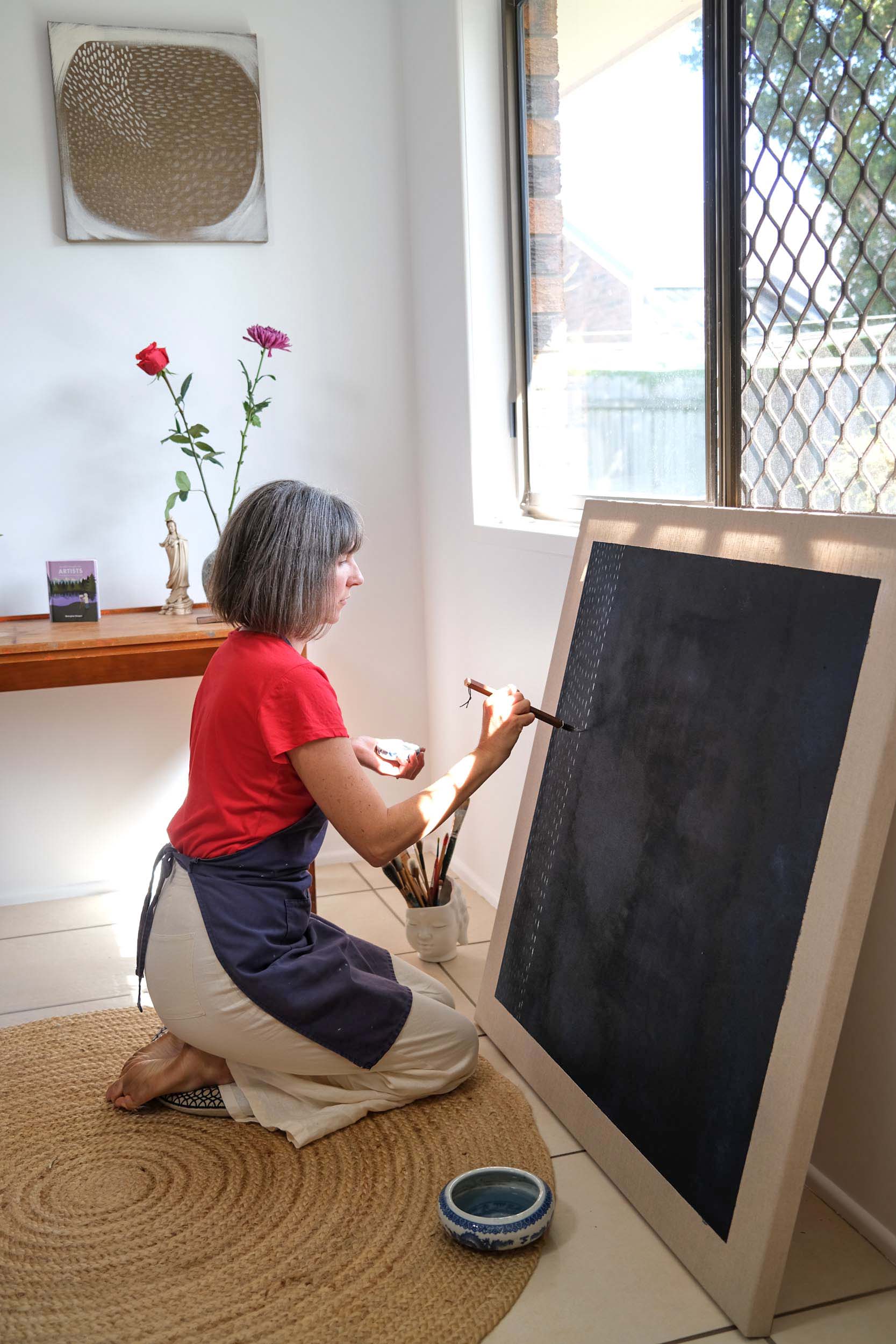 Artist Georgina Hooper painting on a dark indigo canvas.