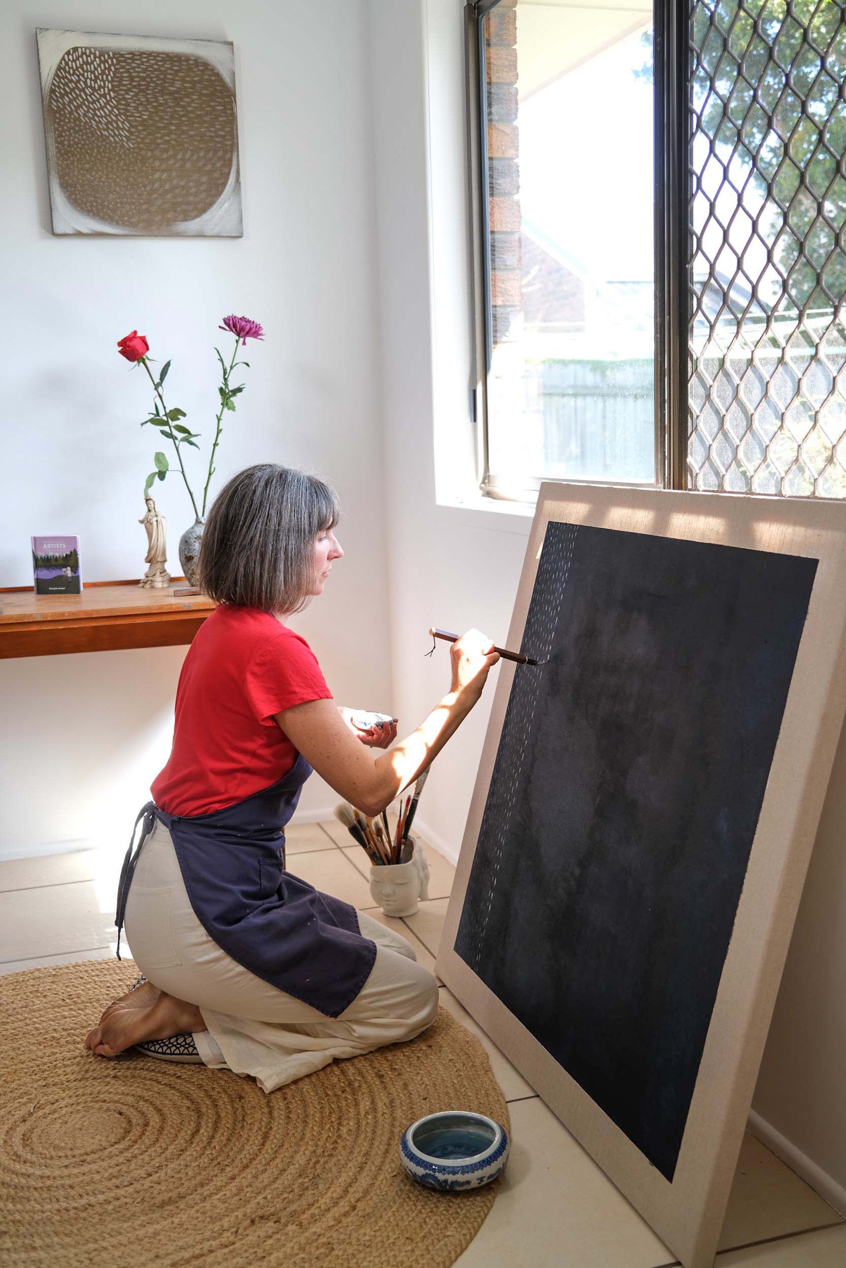 Artist Georgina Hooper painting on a dark indigo canvas.