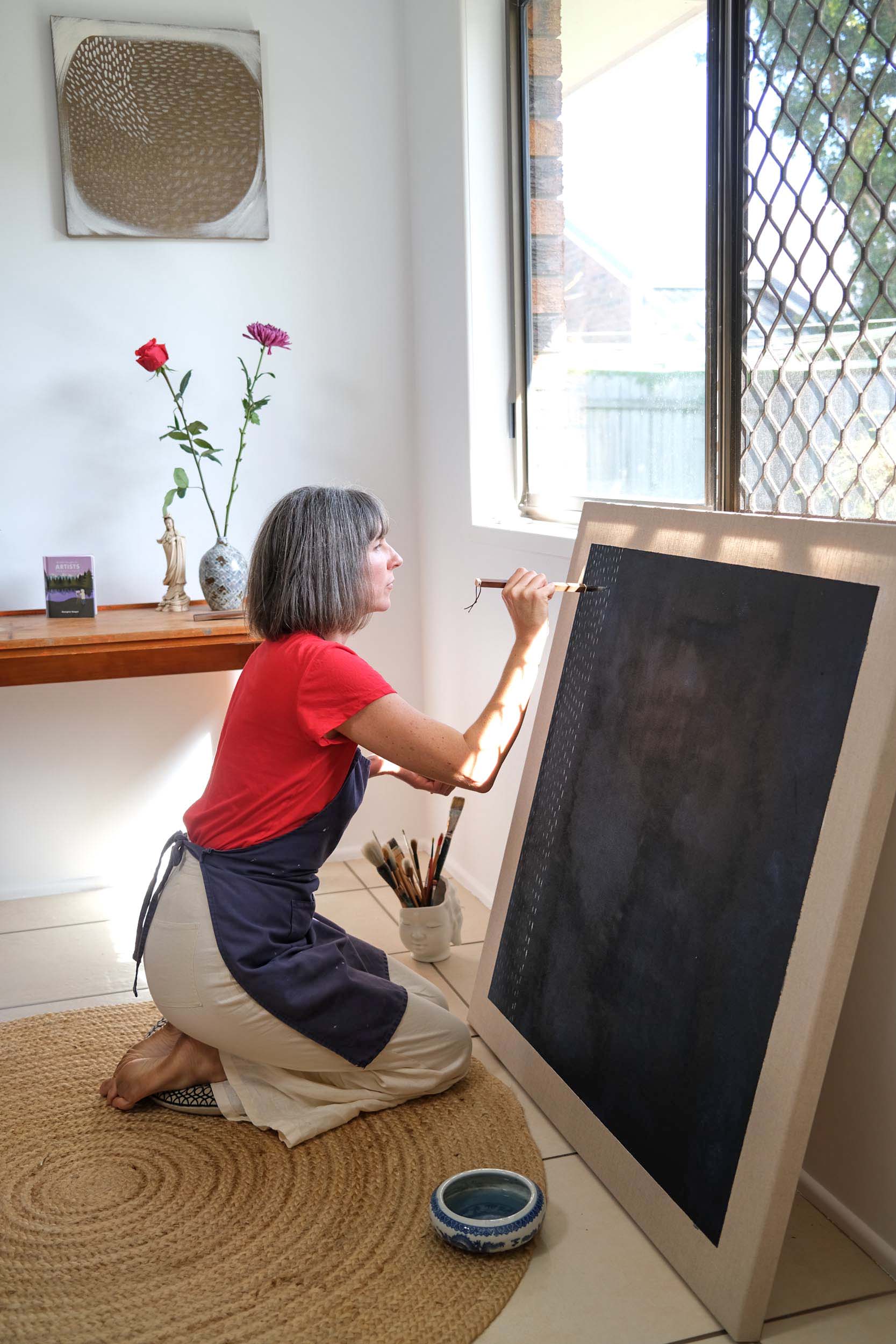 Artist Georgina Hooper painting on a dark indigo canvas.