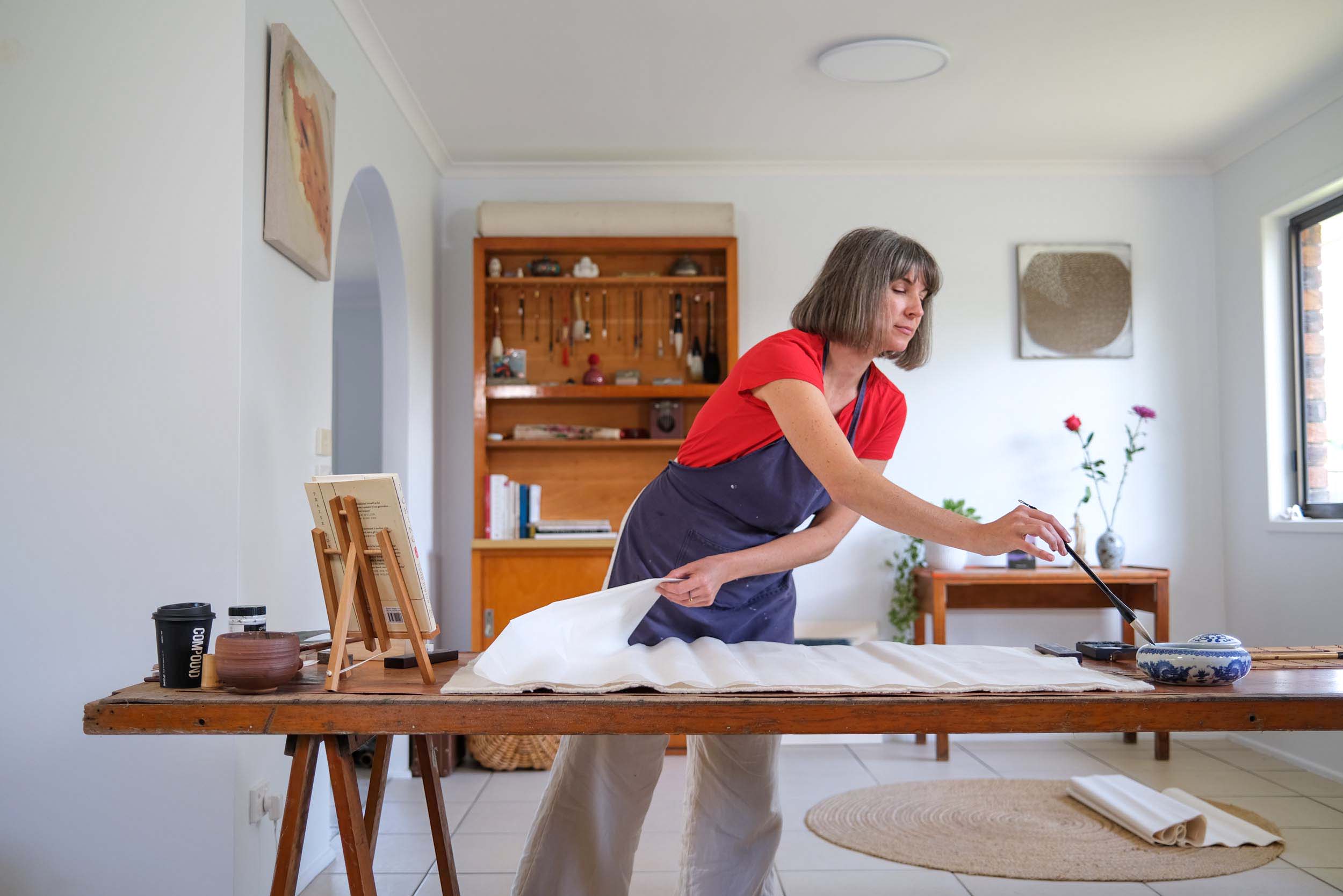 Artist Georgina Hooper painting at her wooden workbench in her sunny studio.