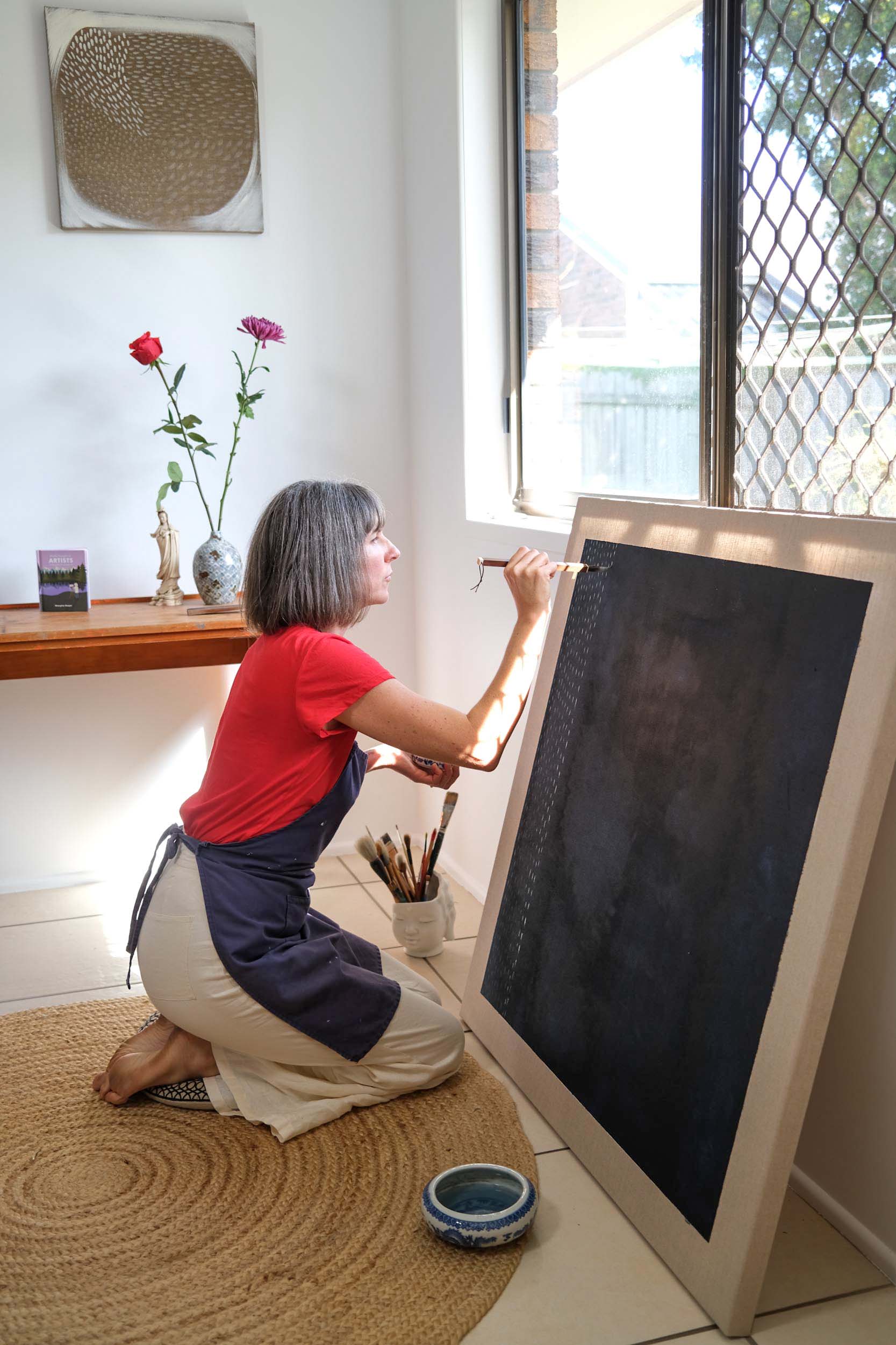Artist Georgina Hooper painting on a dark indigo canvas.