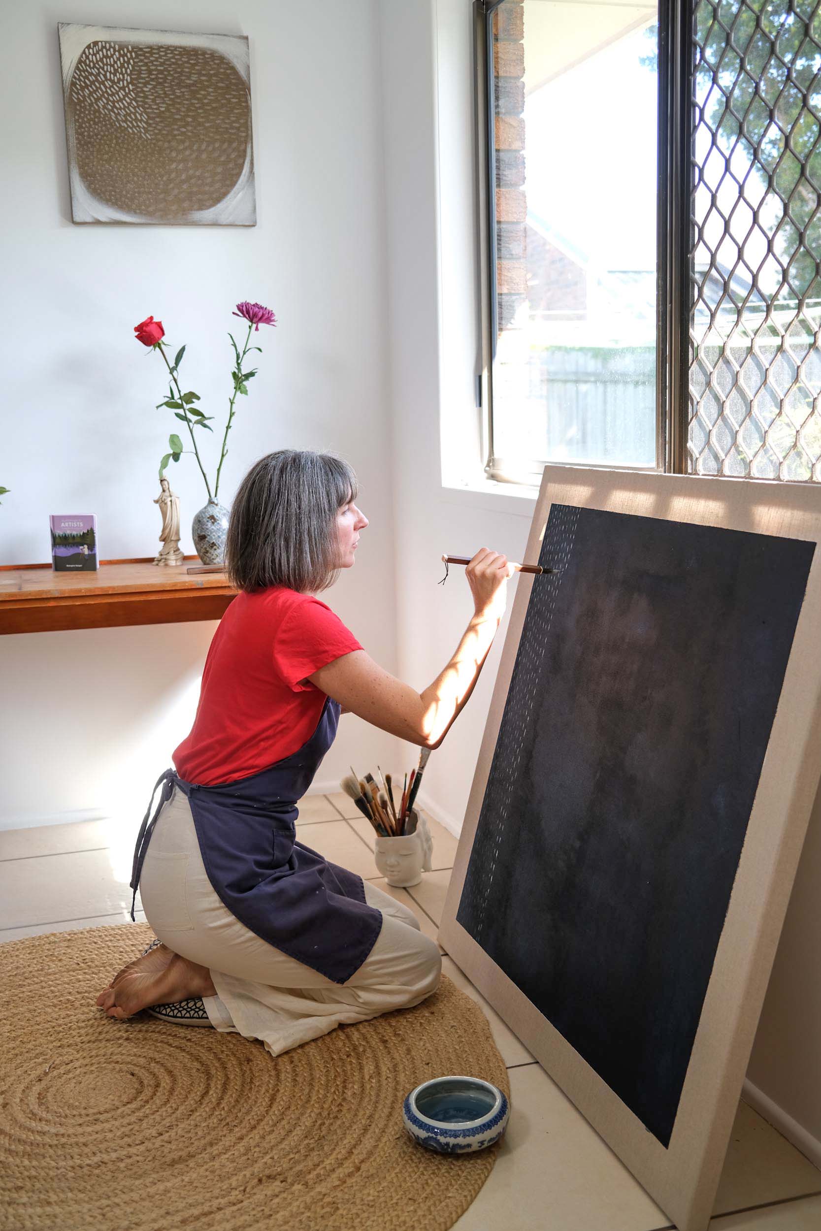 Artist Georgina Hooper painting on a dark indigo canvas.