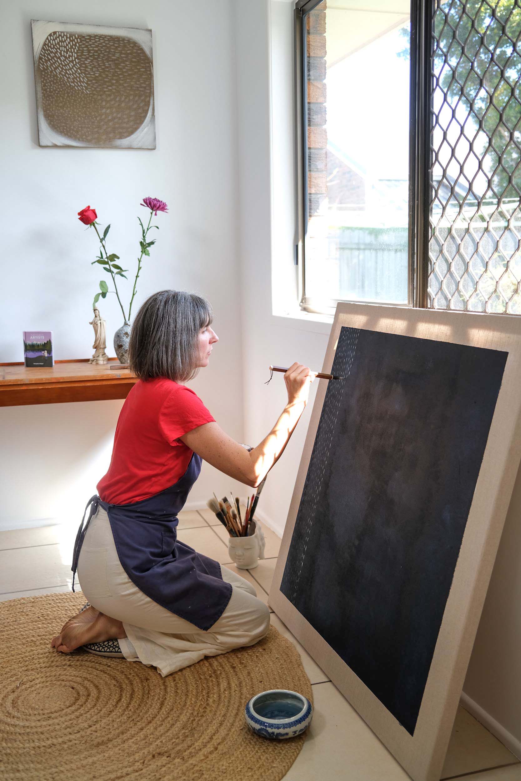 Artist Georgina Hooper painting on a dark indigo canvas.