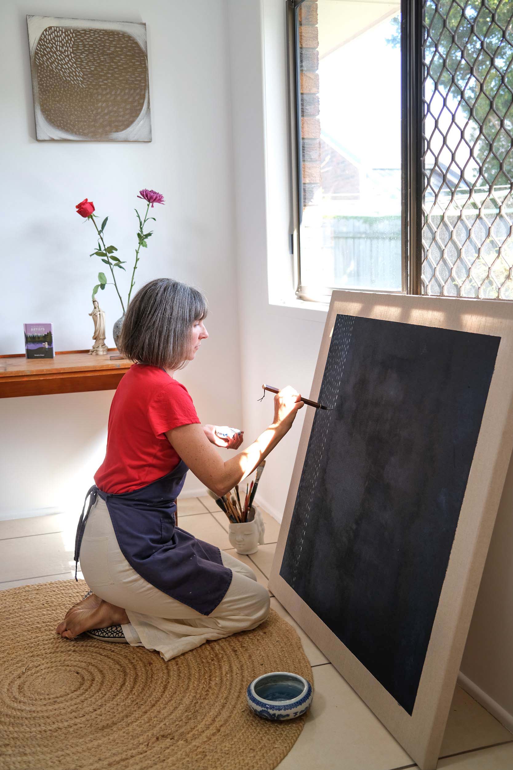 Artist Georgina Hooper painting on a dark indigo canvas.