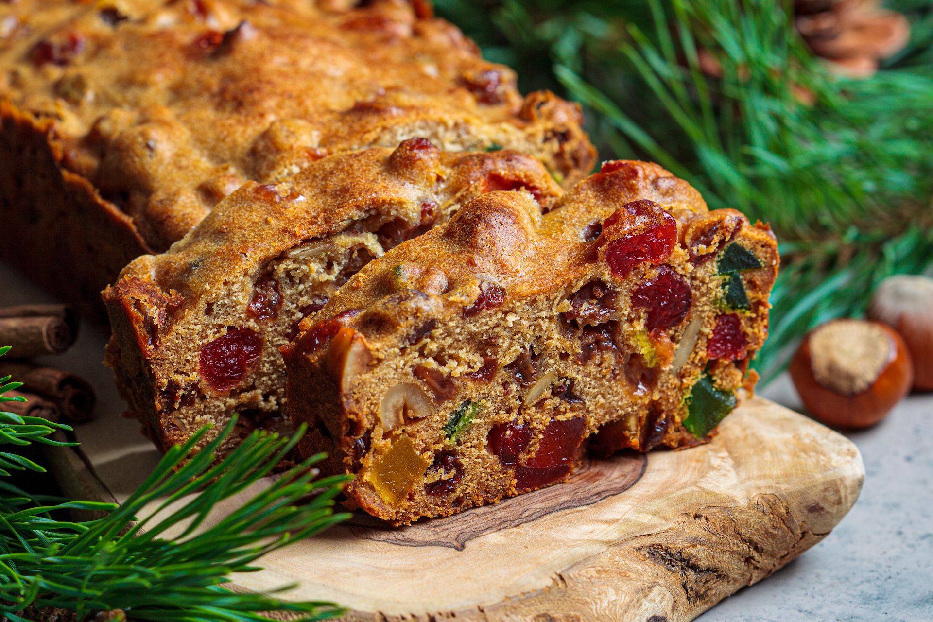 Traditional Christmas fruit cake on a wooden board with festive decorations against a dark background.
