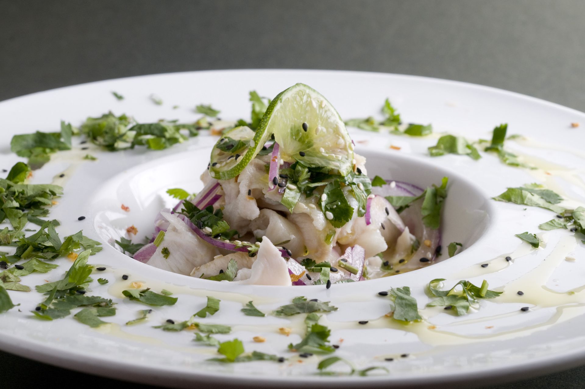 Fish ceviche in a white bowl, topped with lime and fresh herbs.